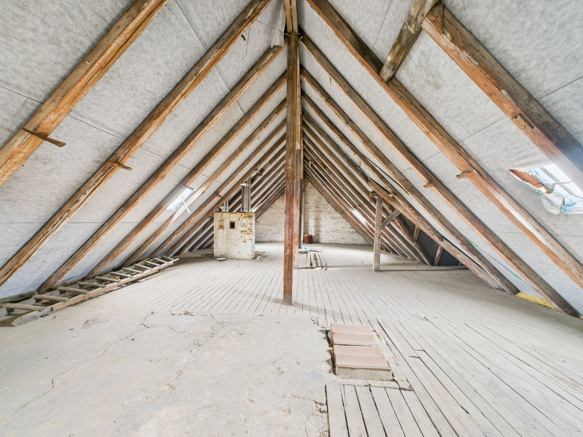 Großer, leerer Dachboden mit Holzbalken und Holzfußboden, Tageslicht durch Dachfenster.