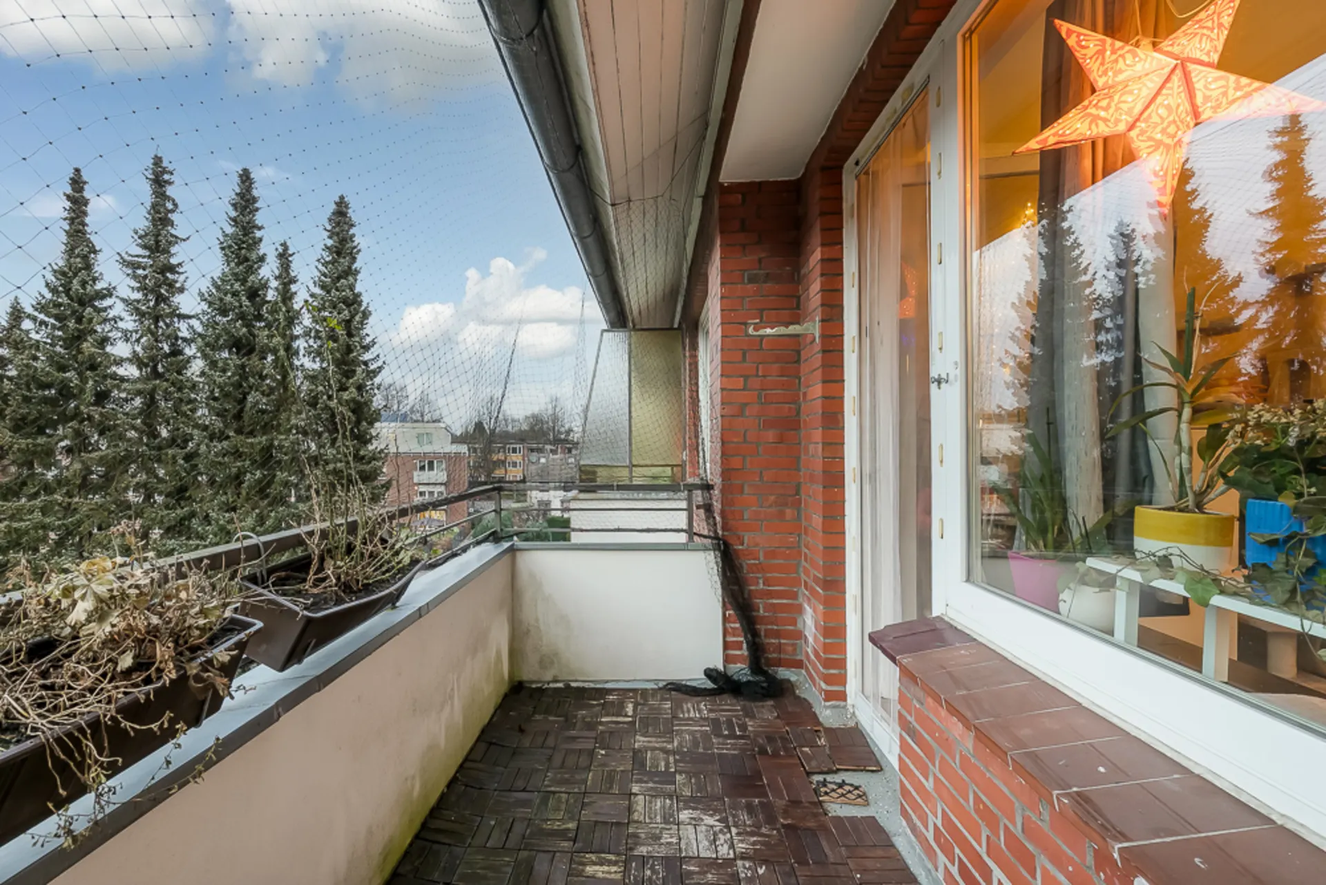 Balkon mit Holzboden, Pflanzkästen und Blick auf Tannenbäume, Fenster mit Sternenlampe.
