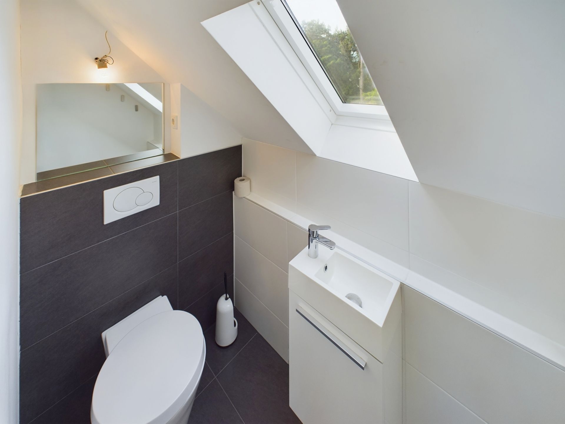Modernes kleines Badezimmer mit Toilette, Waschbecken, Spiegel und Dachfenster.