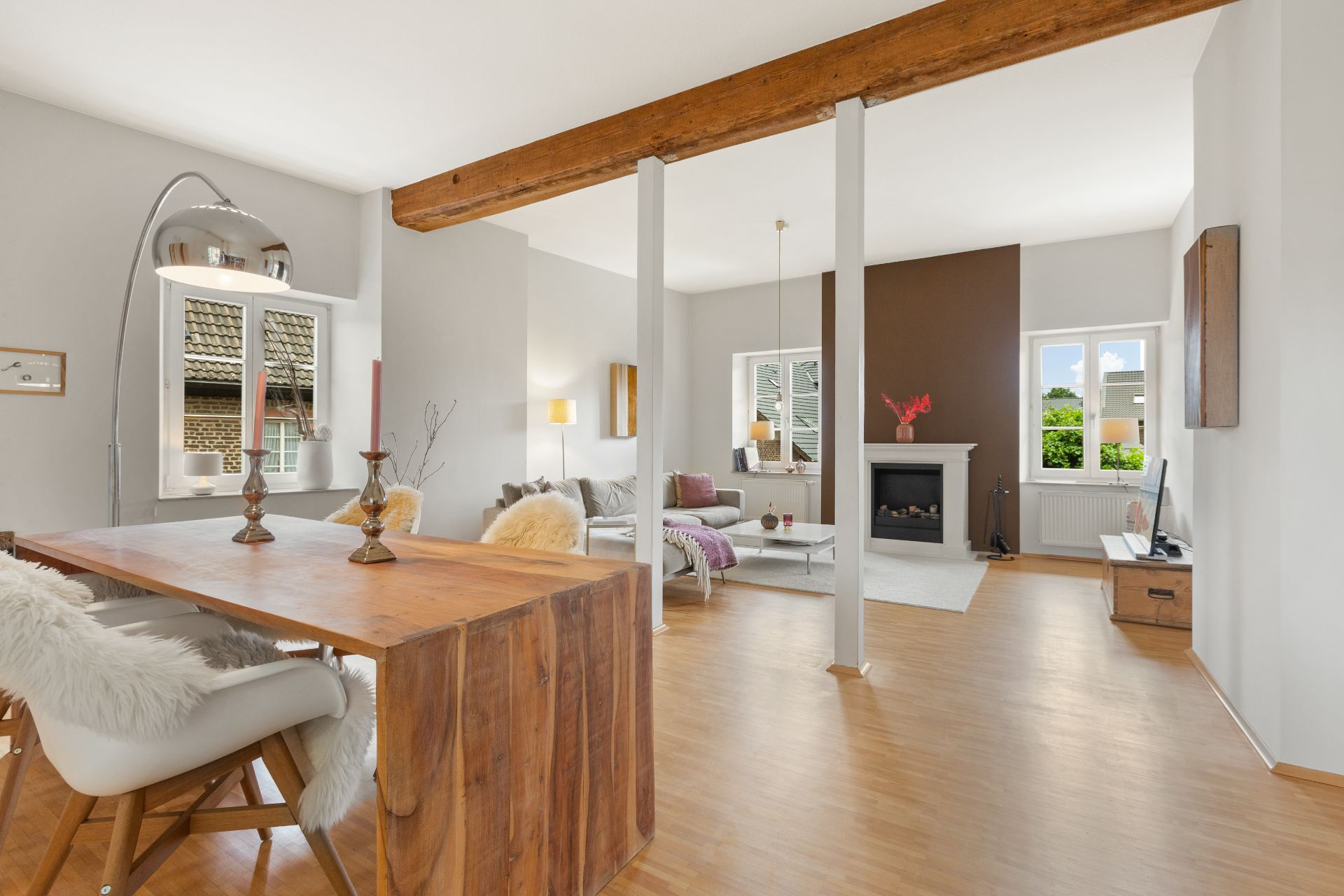 Helles Wohnzimmer mit Holztisch, Kamin, Sofa, Fernseher und großen Fenstern.