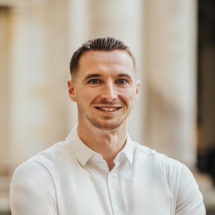 Ein Mann mit weißem Hemd steht mit verschränkten Armen und lächelt in die Kamera.