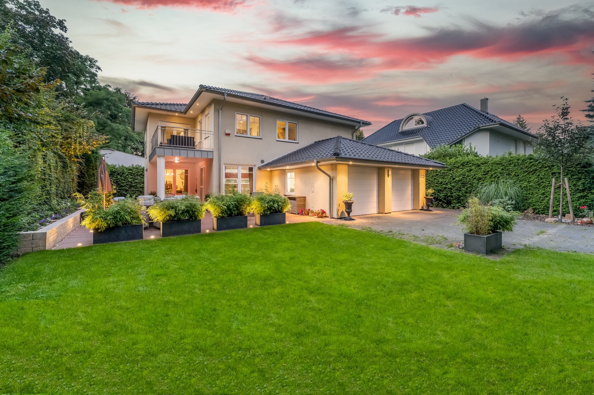 Modernes zweistöckiges Wohnhaus mit großem Garten, Terrasse und Doppelgarage bei Sonnenuntergang.