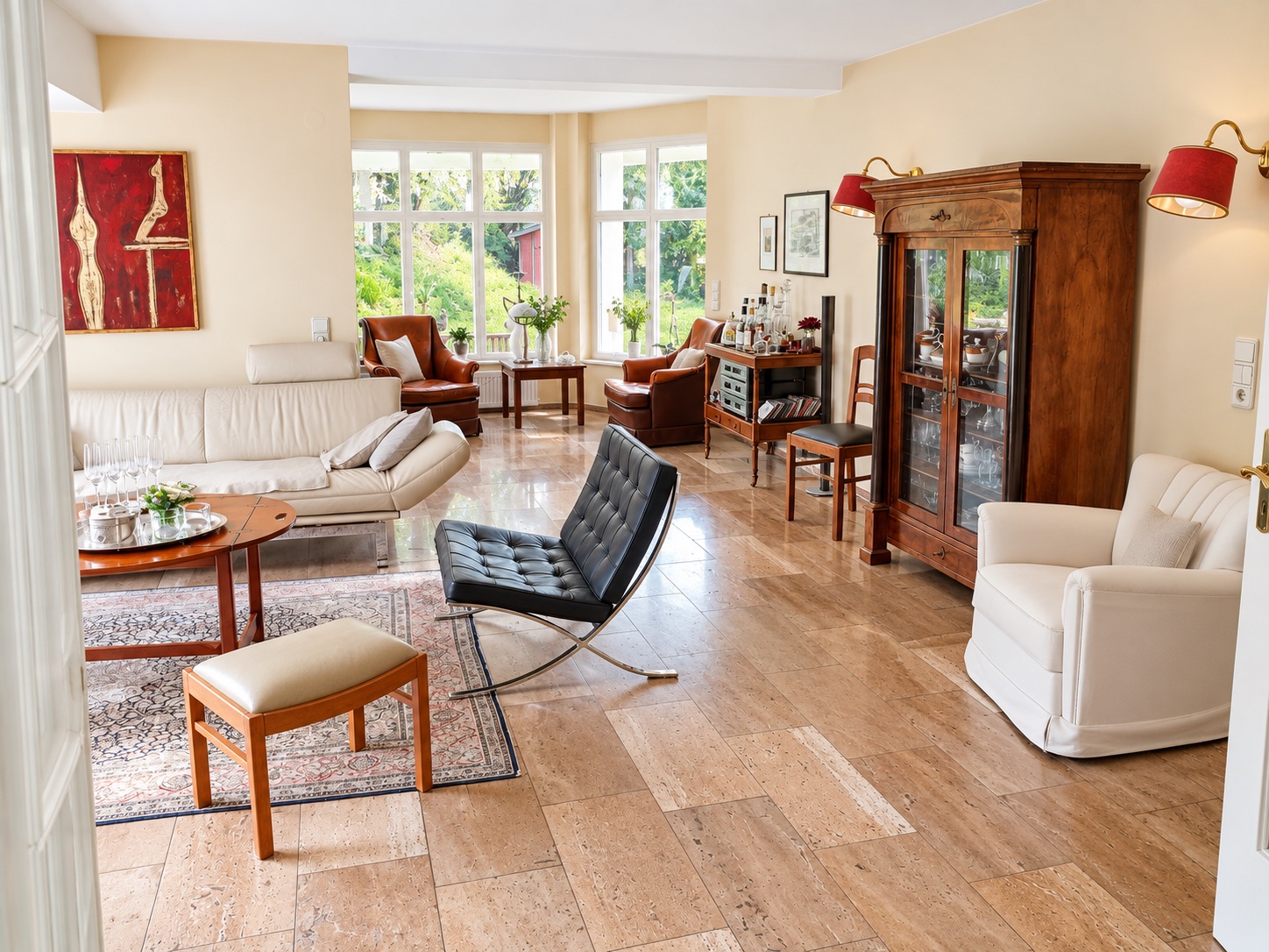 Helles Wohnzimmer mit Ledersofa, Sessel, Glastürschrank und großen Fenstern.