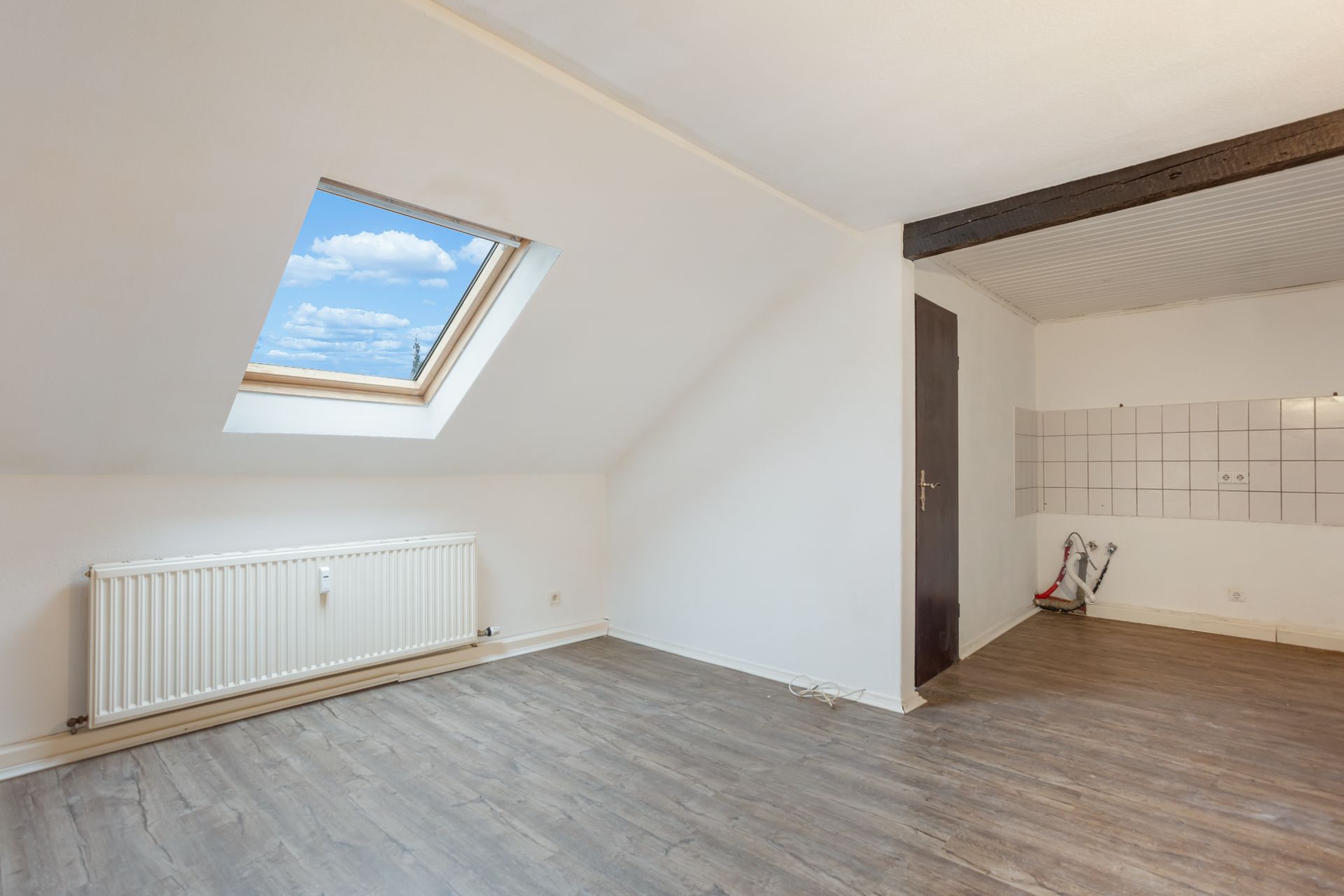 Heller Raum mit Dachfenster, Holzfußboden, Heizung und gefliestem Wandbereich.
