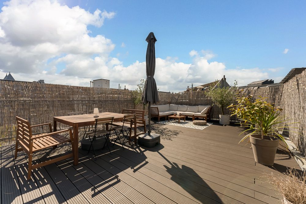 Dachterrasse mit Holztisch, Stühlen, Sitzbank, Sofaecke, Pflanzen und Sonnenschirm.
