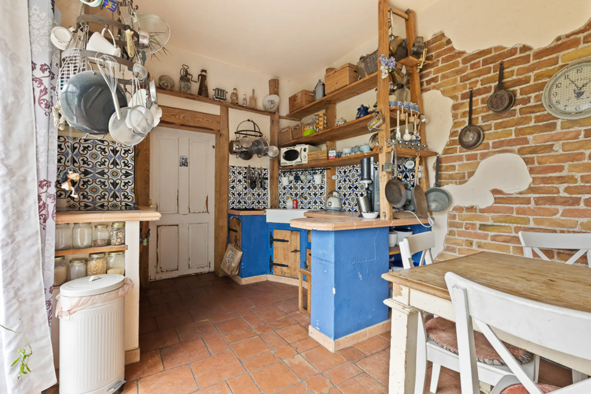 Küche mit gemusterten Fliesen, offenen Regalen und Holztisch mit Stühlen.