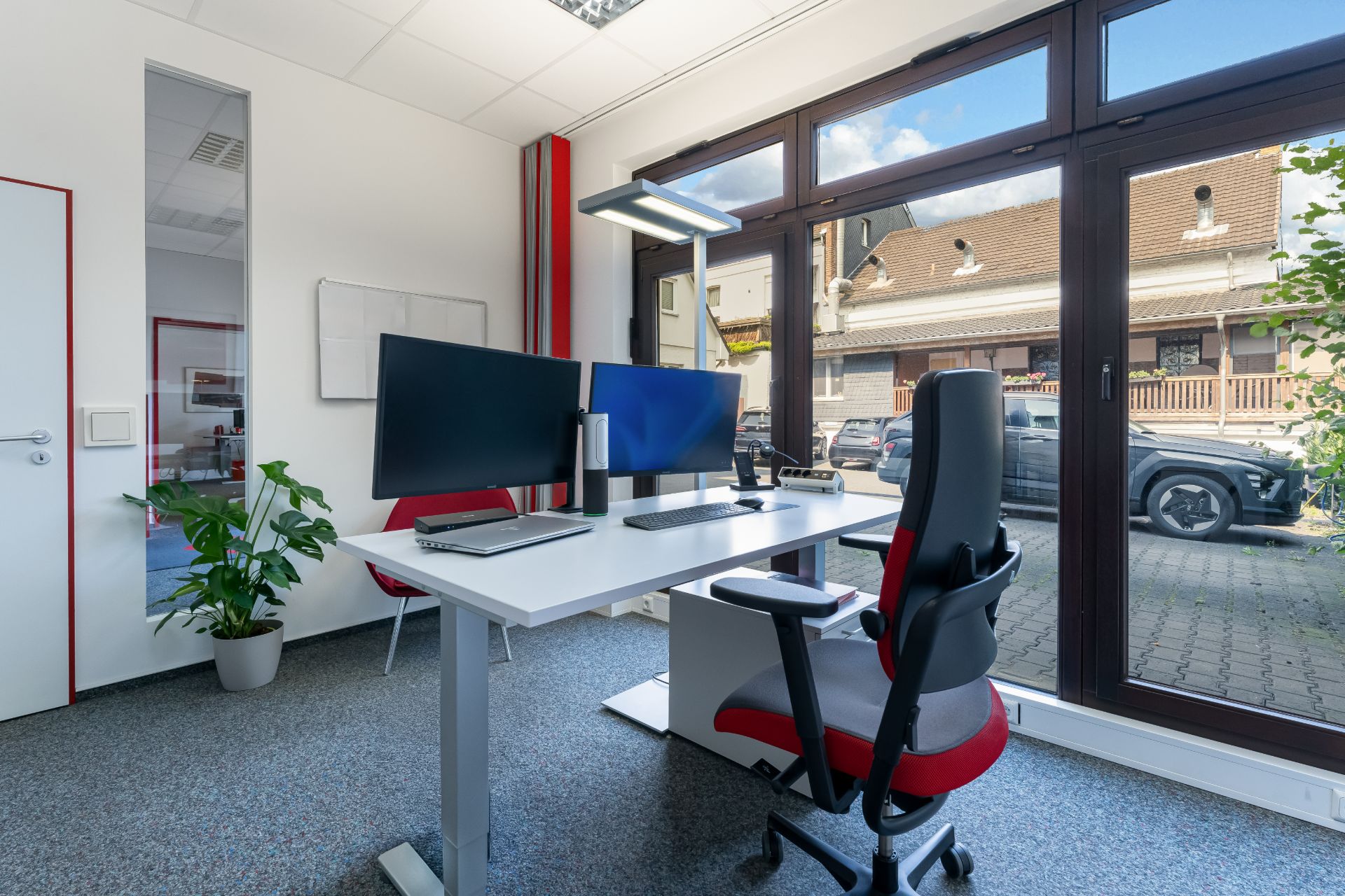 Modernes Arbeitszimmer mit Schreibtisch, zwei Monitoren und großem Fenster mit Blick nach draußen.