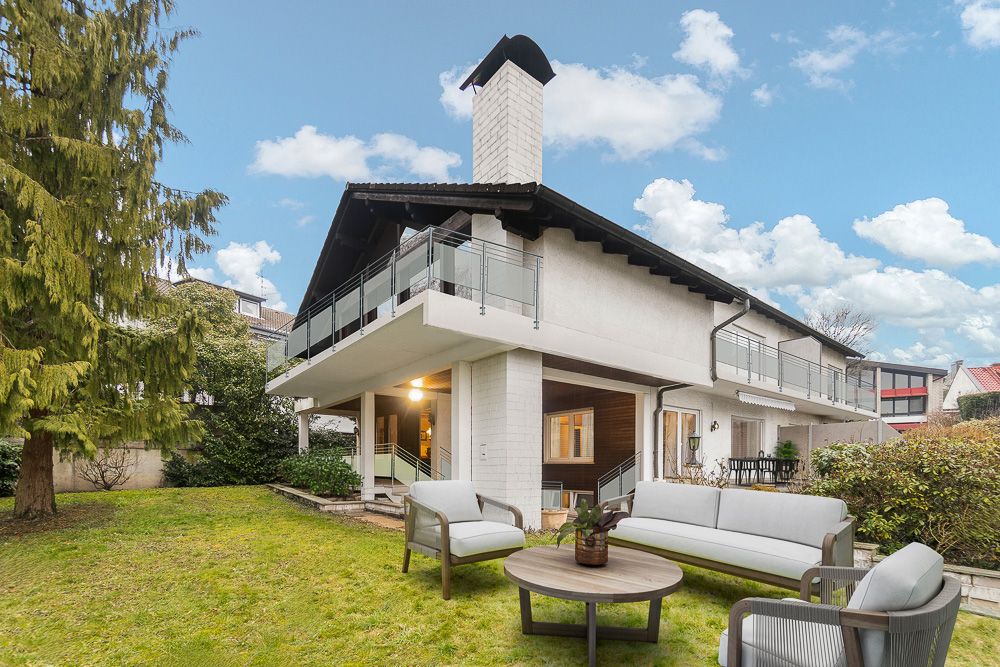 Modernes Wohnhaus mit Balkon und Terrasse, Gartenmöbeln und Rasen im Vorgarten.
