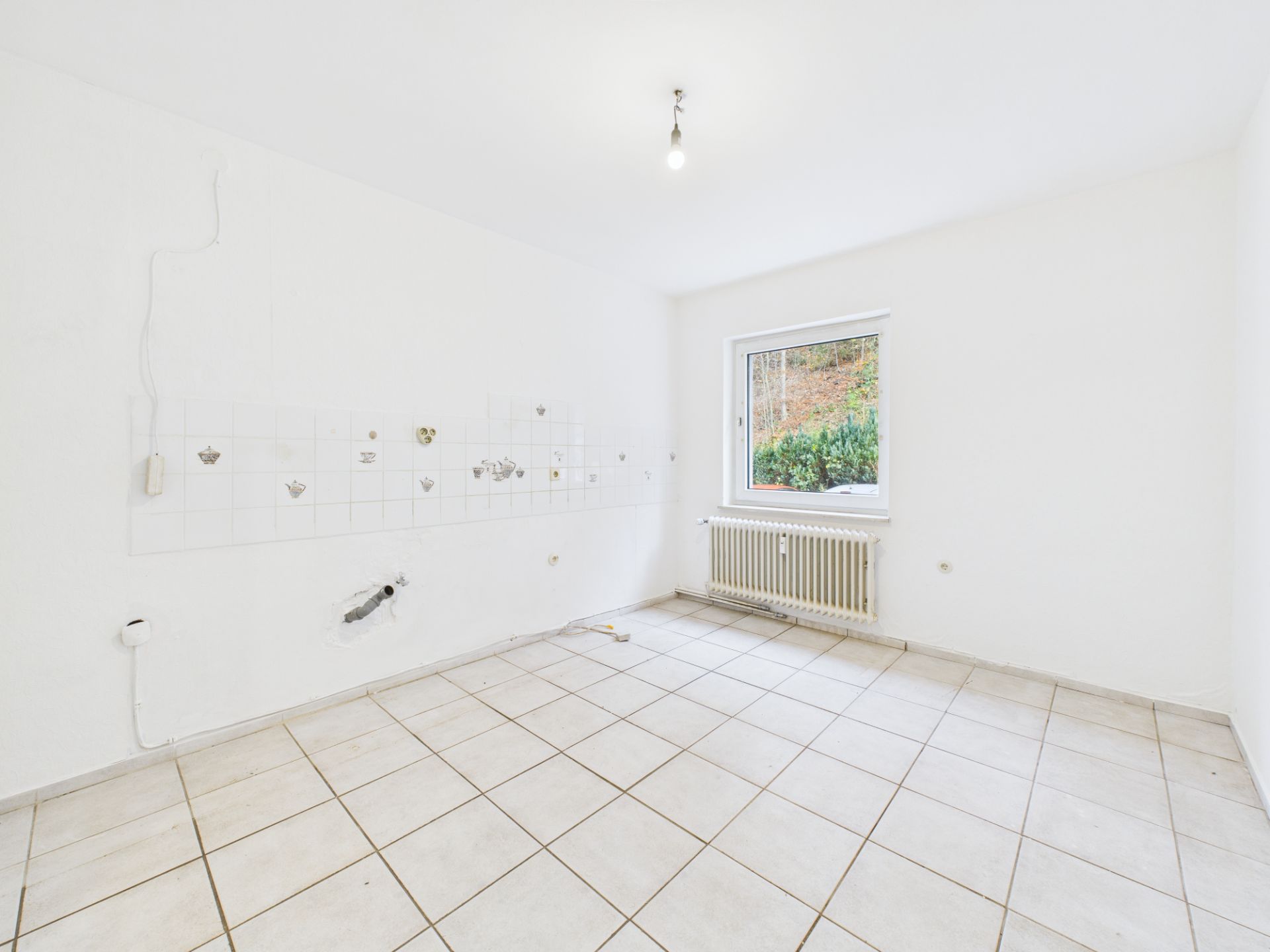 Leerer, weißer Raum mit Fliesenboden, Fenster und Heizkörper unter dem Fenster.