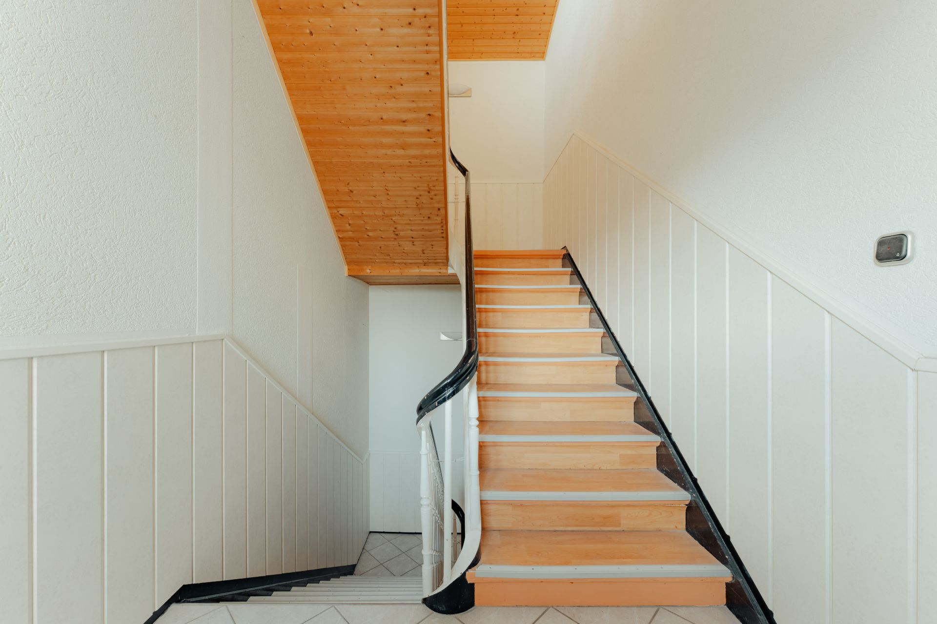 Helle Holztreppe mit weißem Geländer und Holzdecke in einem Wohnhaus.