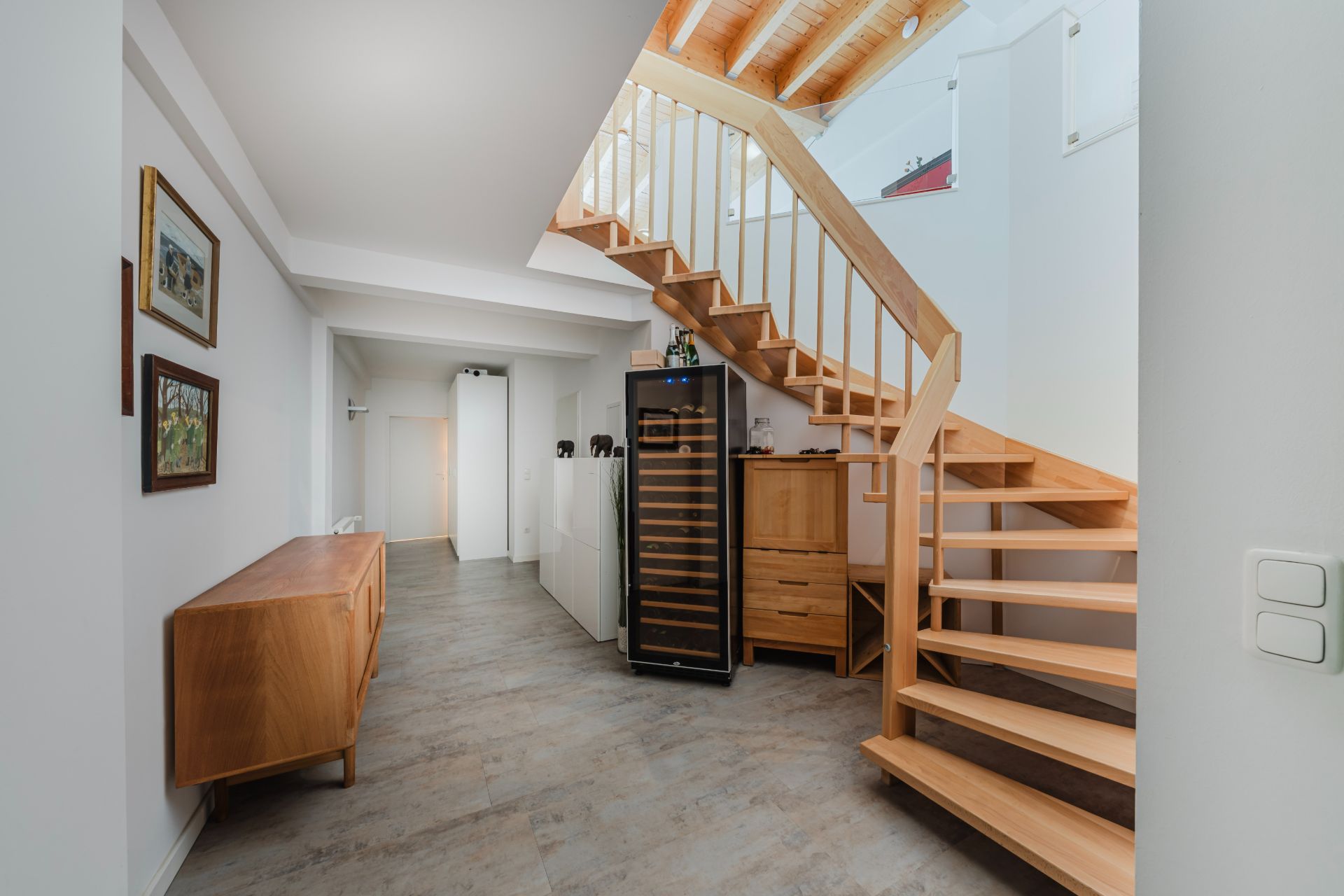 Flur mit Holztreppe, Holzkommode, Weinschrank und Bilderrahmen an der Wand.