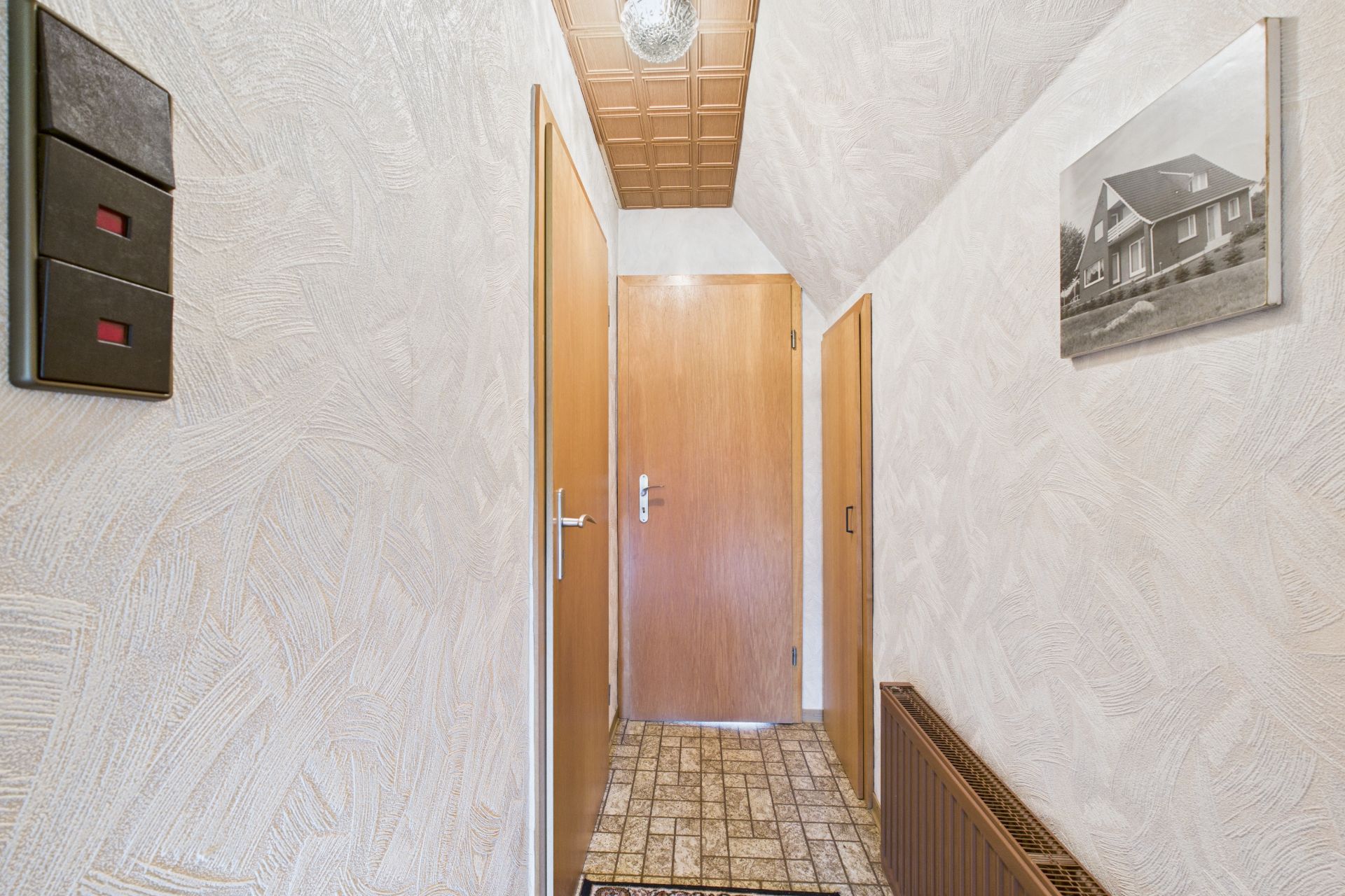 Schmaler Flur mit Holztüren, Heizung, Lichtschalter und Bild an der Wand.