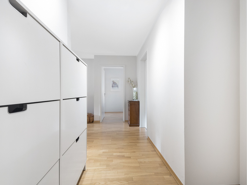 Heller Flur mit Holzboden, weißen Wänden und weißen Schränken links.