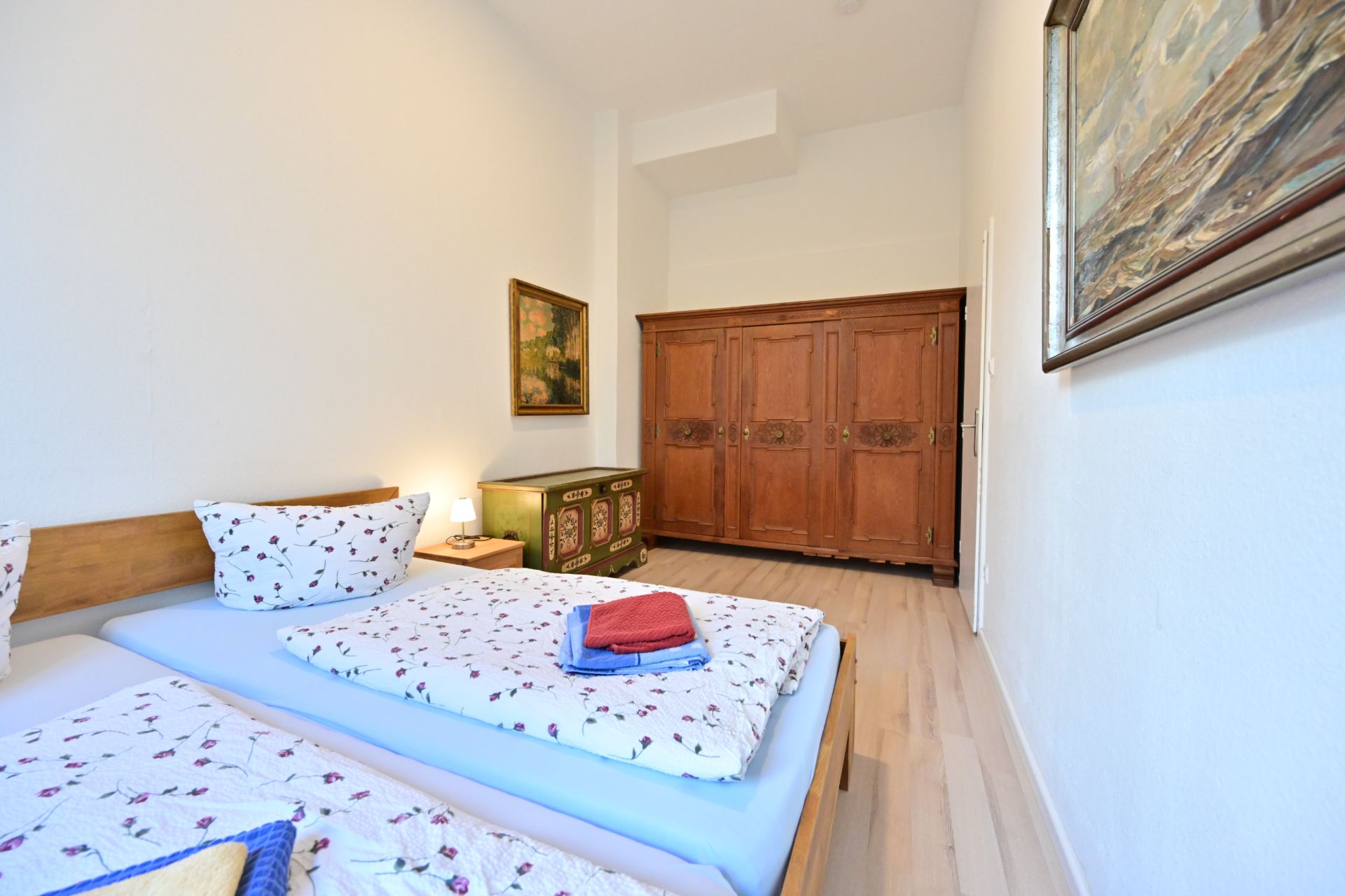 Schlafzimmer mit zwei Einzelbetten, Holzmöbeln, Gemälden an den Wänden und Holzboden.
