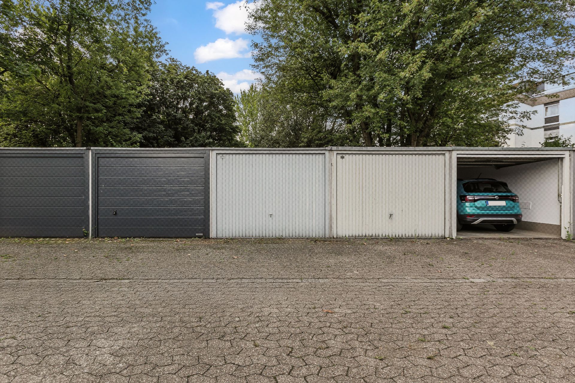 Reihe von Garagen, eine Garage ist geöffnet und darin steht ein Auto. Bäume im Hintergrund.