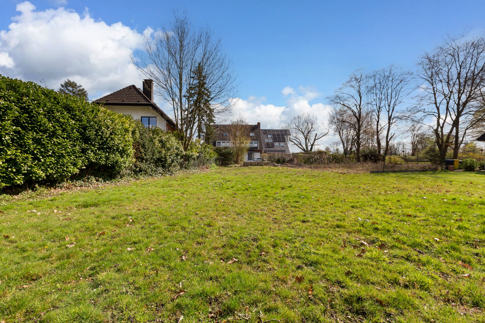 Großer Garten mit Rasenfläche, Büschen und einigen Bäumen, im Hintergrund ein Wohnhaus.