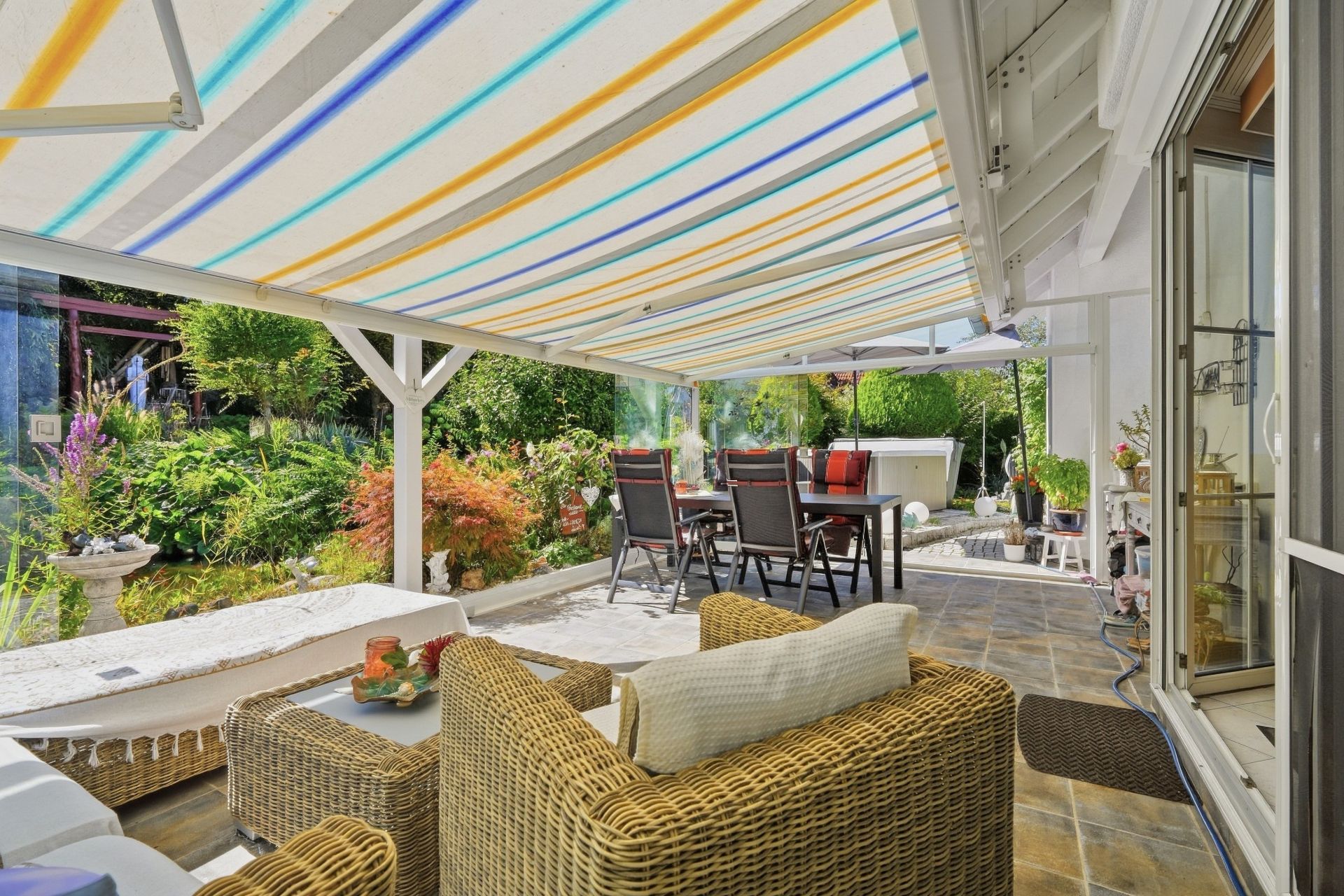 Überdachte Terrasse mit Sitzgruppe, Esstisch und Blick auf einen Garten.