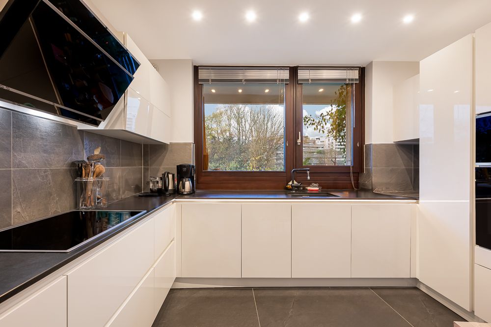 Moderne Küche mit weißen Schränken, grauen Fliesen und großem Fenster mit Blick nach draußen.