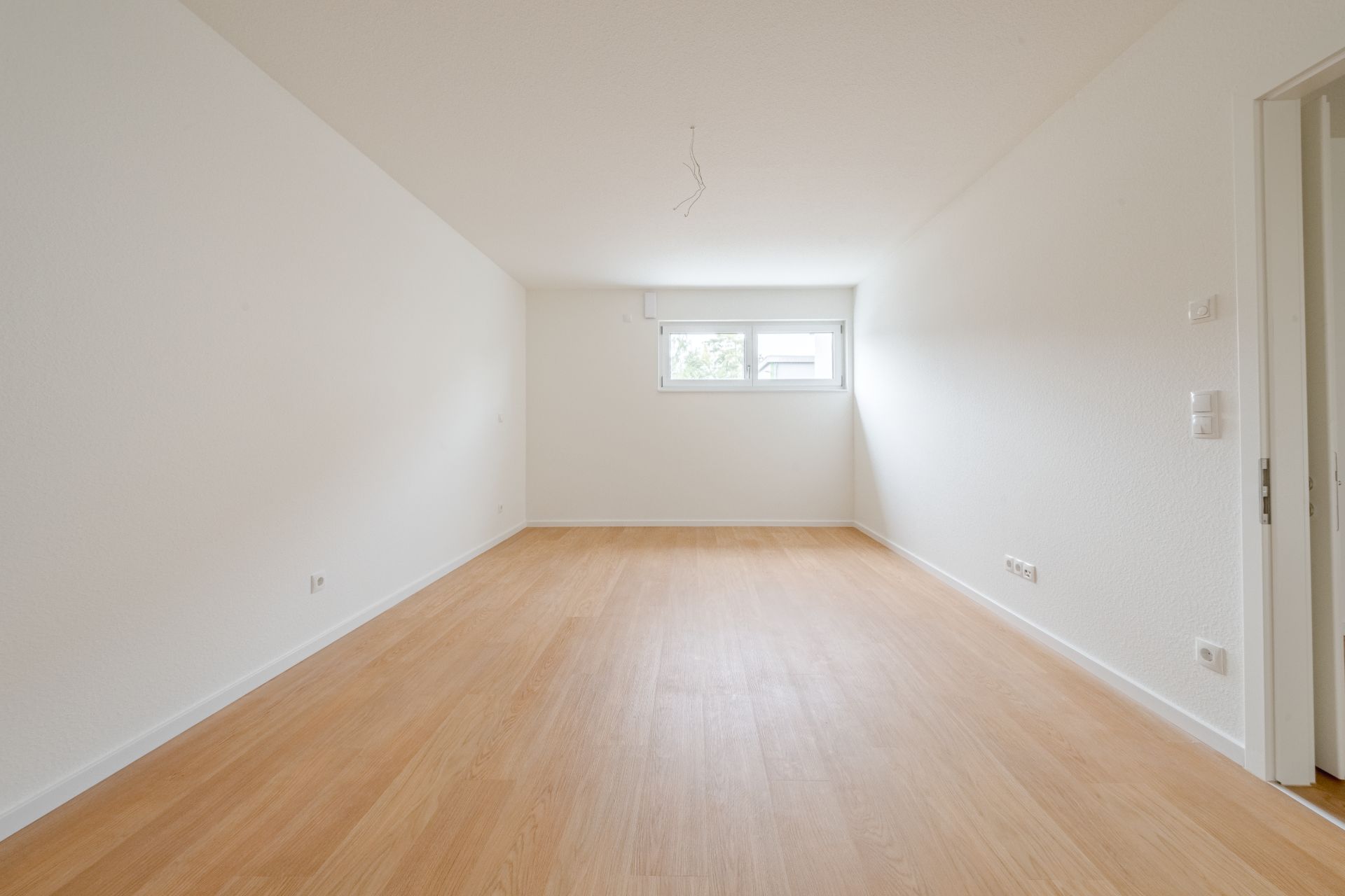 Leerer Raum mit hellem Holzboden und zwei Fenstern an der Stirnwand.