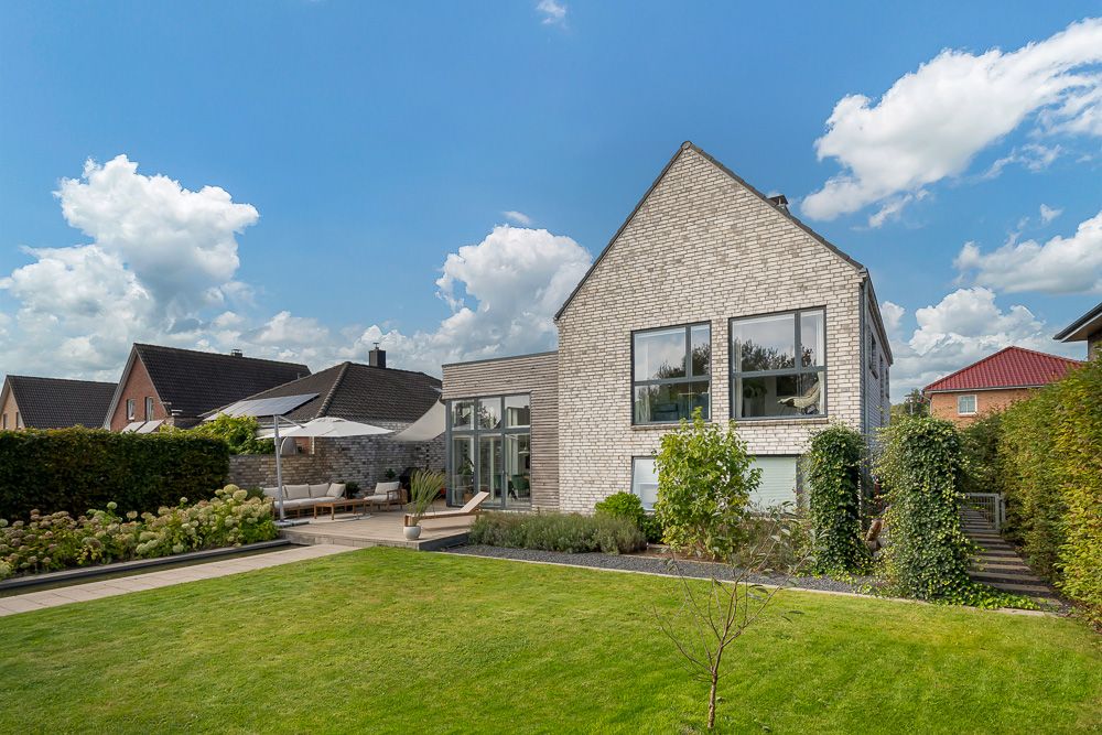 Modernes Einfamilienhaus mit großem Garten, Terrasse und Sonnenschirmen bei Tageslicht.