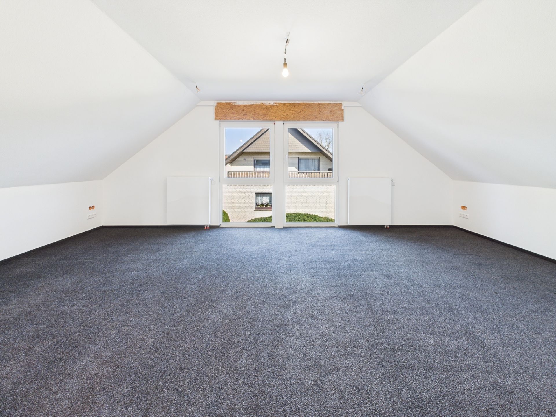 Leerer Dachbodenraum mit grauem Teppich und großen Fenstern, Blick nach draußen.