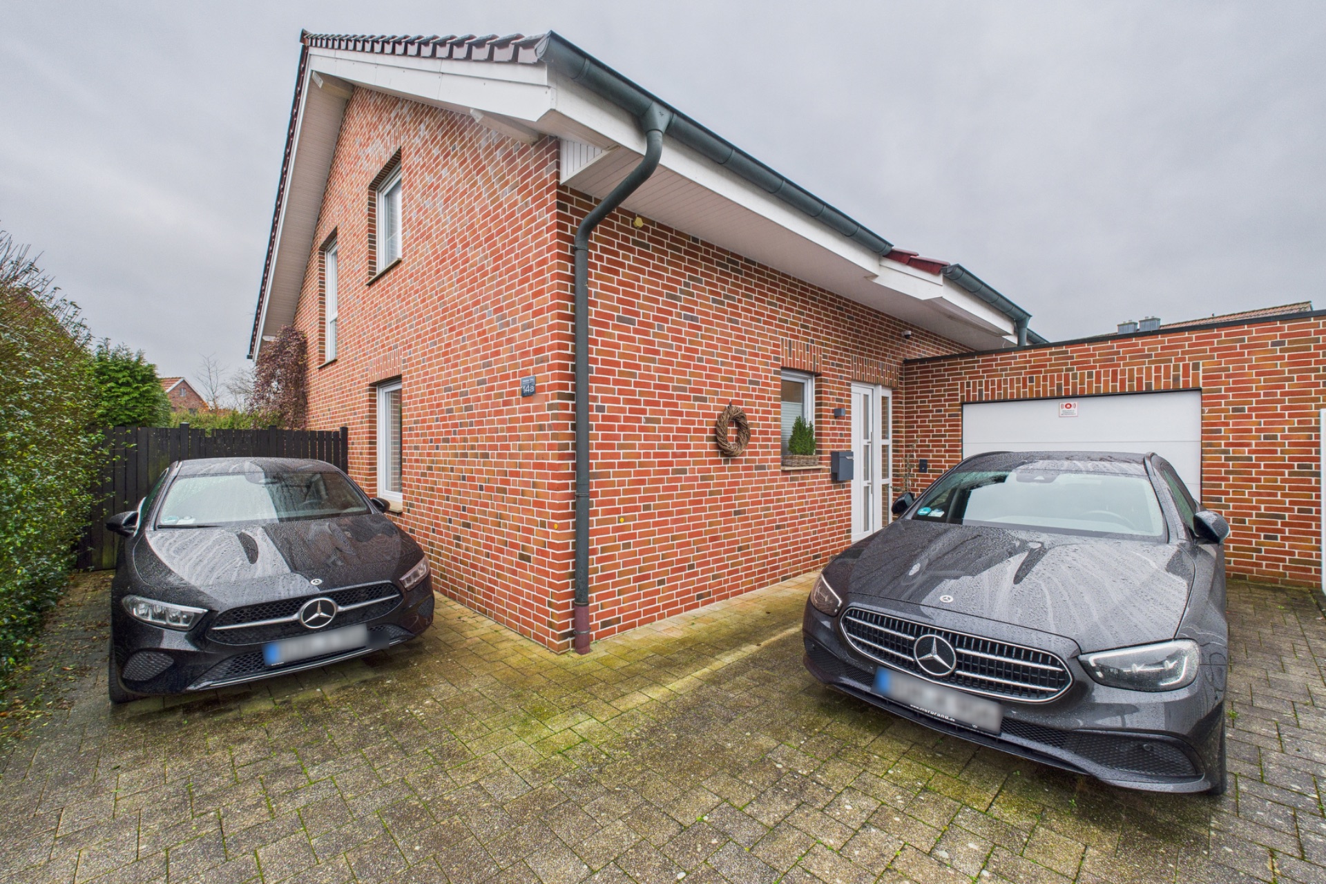 Zwei schwarze Autos stehen auf einer Auffahrt vor einem roten Backsteinhaus mit Garage.