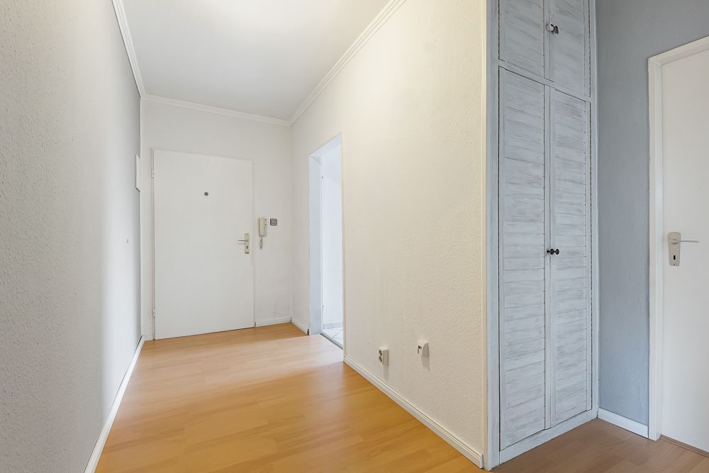 Heller Flur mit Holzboden, weißer Eingangstür und Einbauschrank.