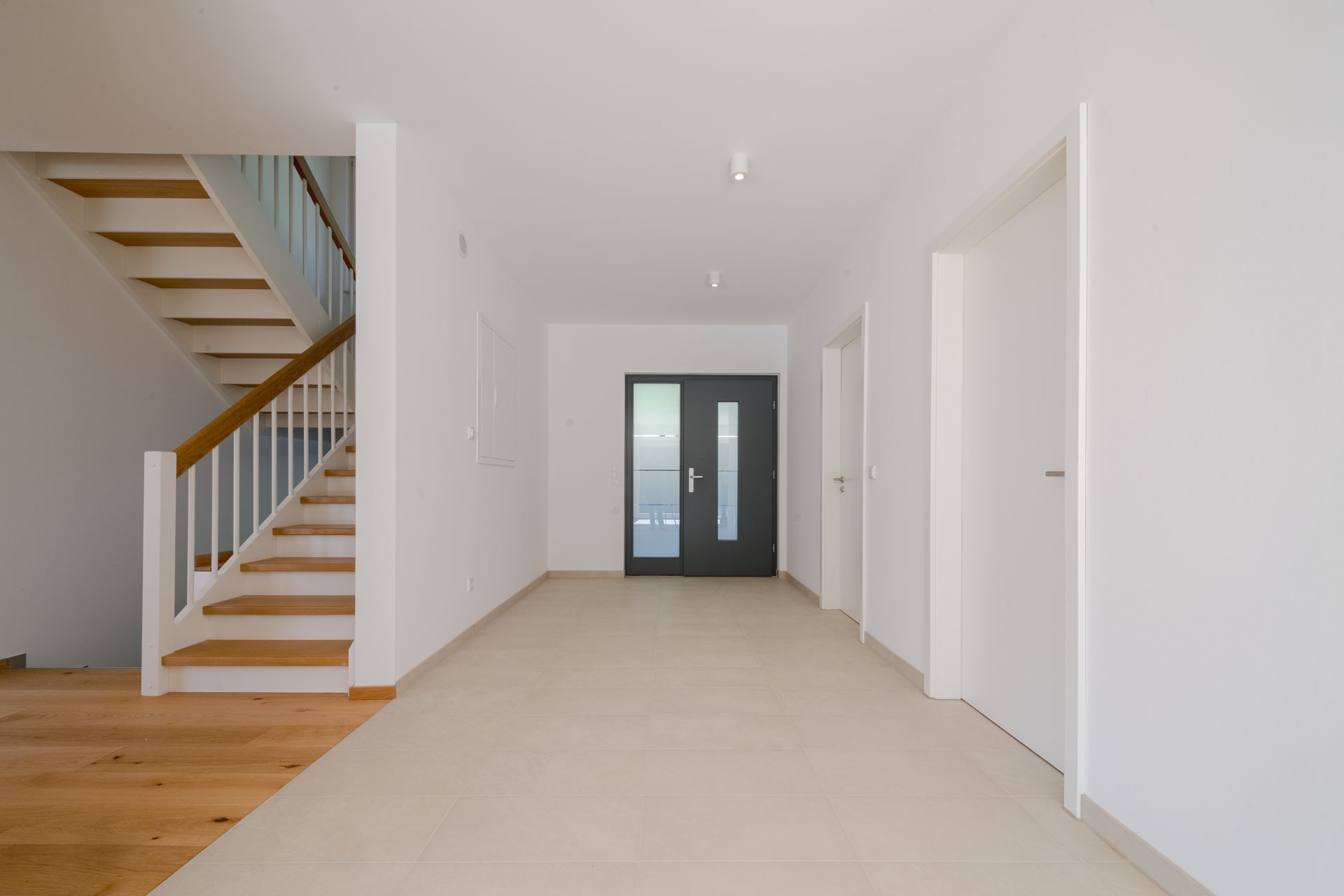 Heller Flur mit Treppe, mehreren Türen und einer dunklen Eingangstür.