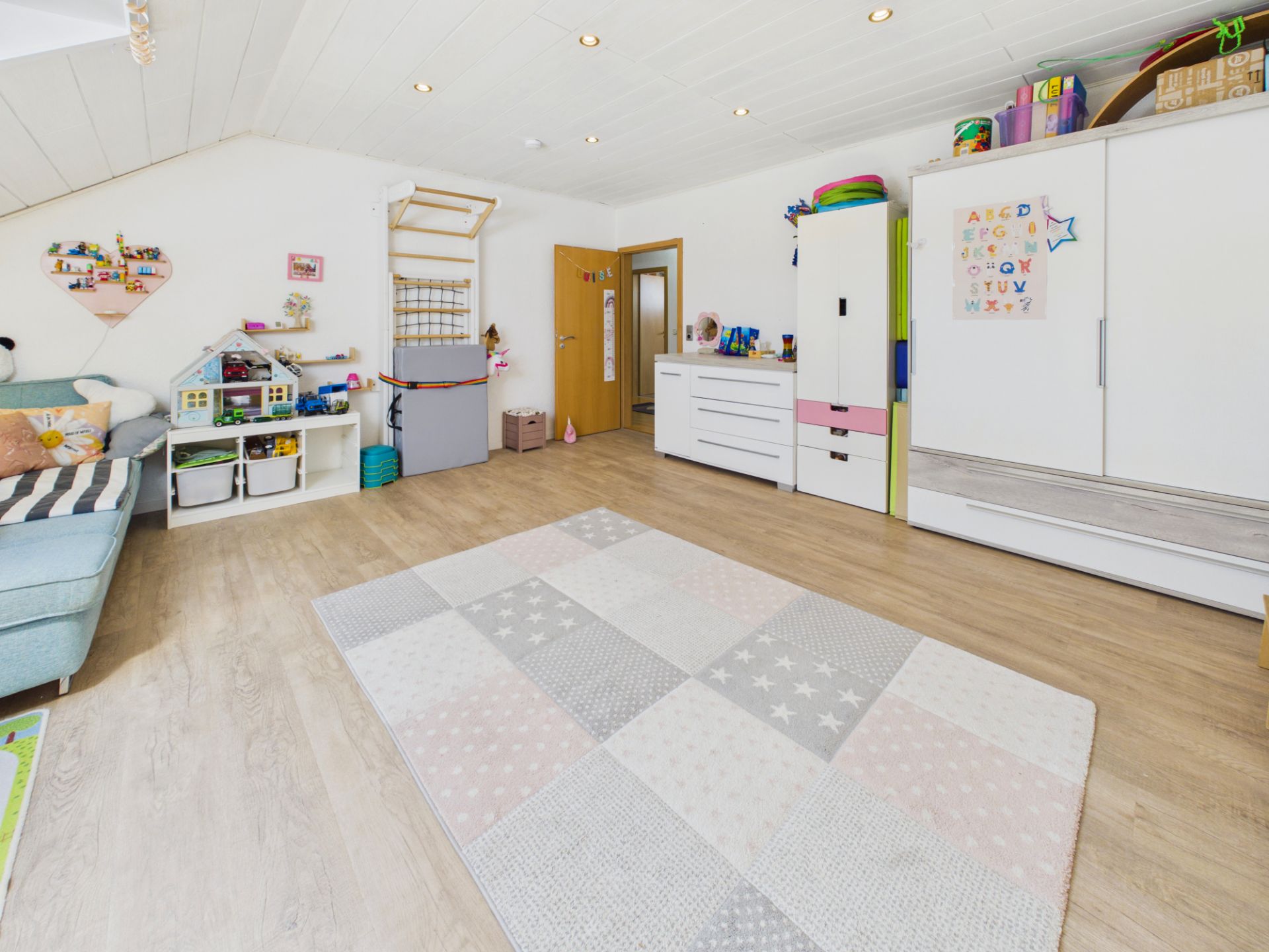 Geräumiges Kinderzimmer mit buntem Teppich, Spielzeugregalen und Spielzeugküche.