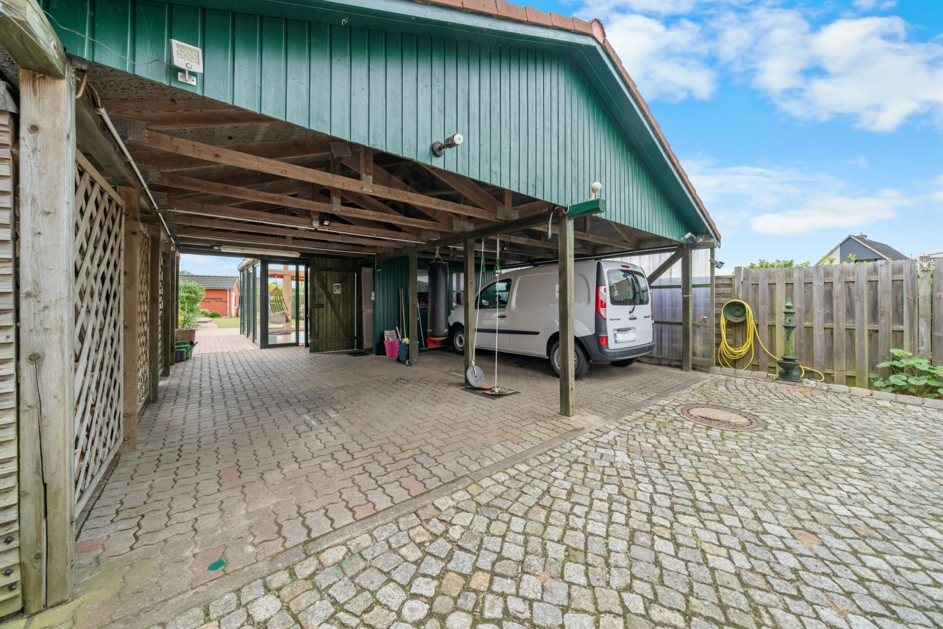 Überdachter Carport mit Pflastersteinen, geparktem weißen Van und Schaukelsitz.