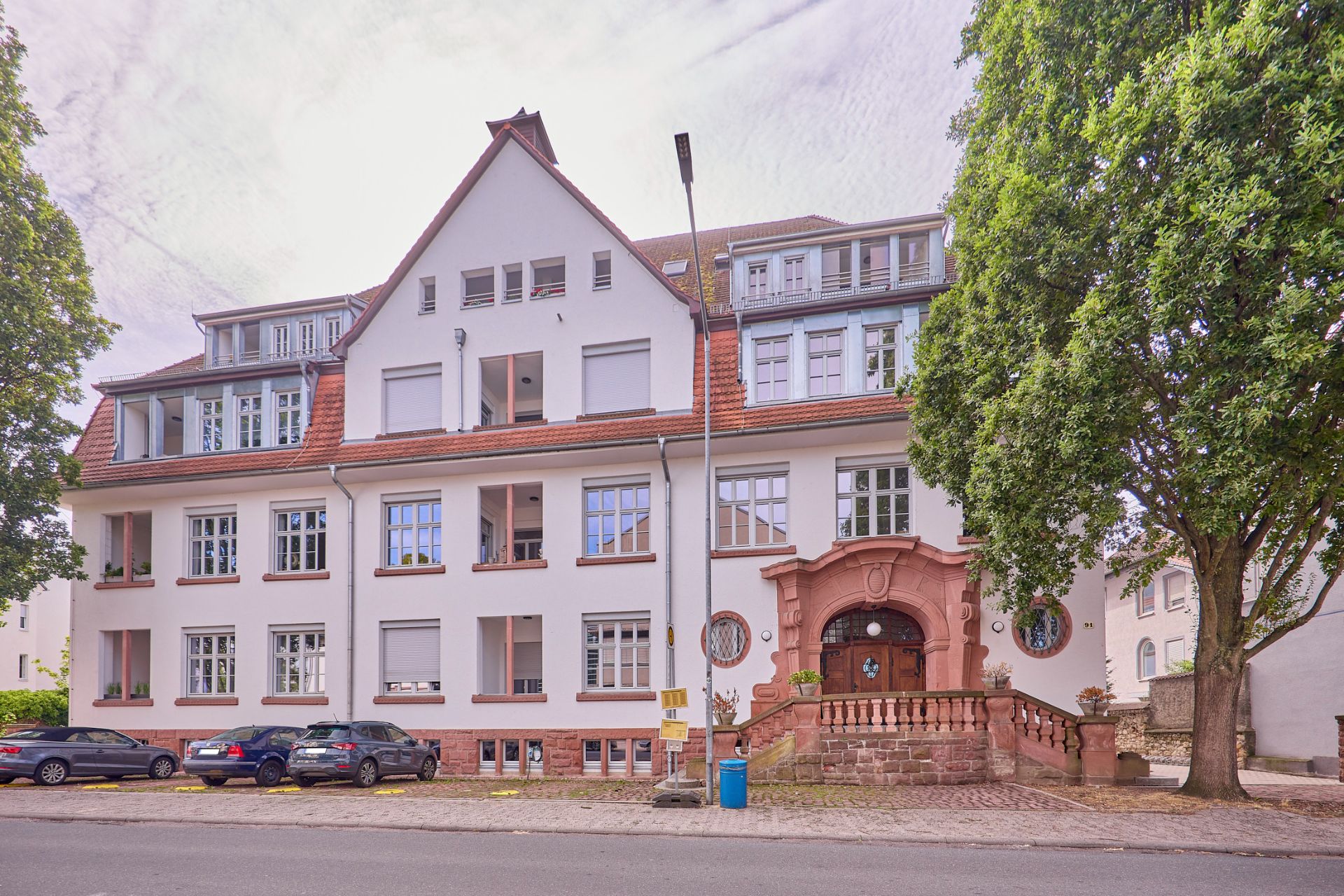 Mehrstöckiges Wohnhaus mit weißer Fassade, roten Fensterrahmen und Eingangsportal aus Stein.