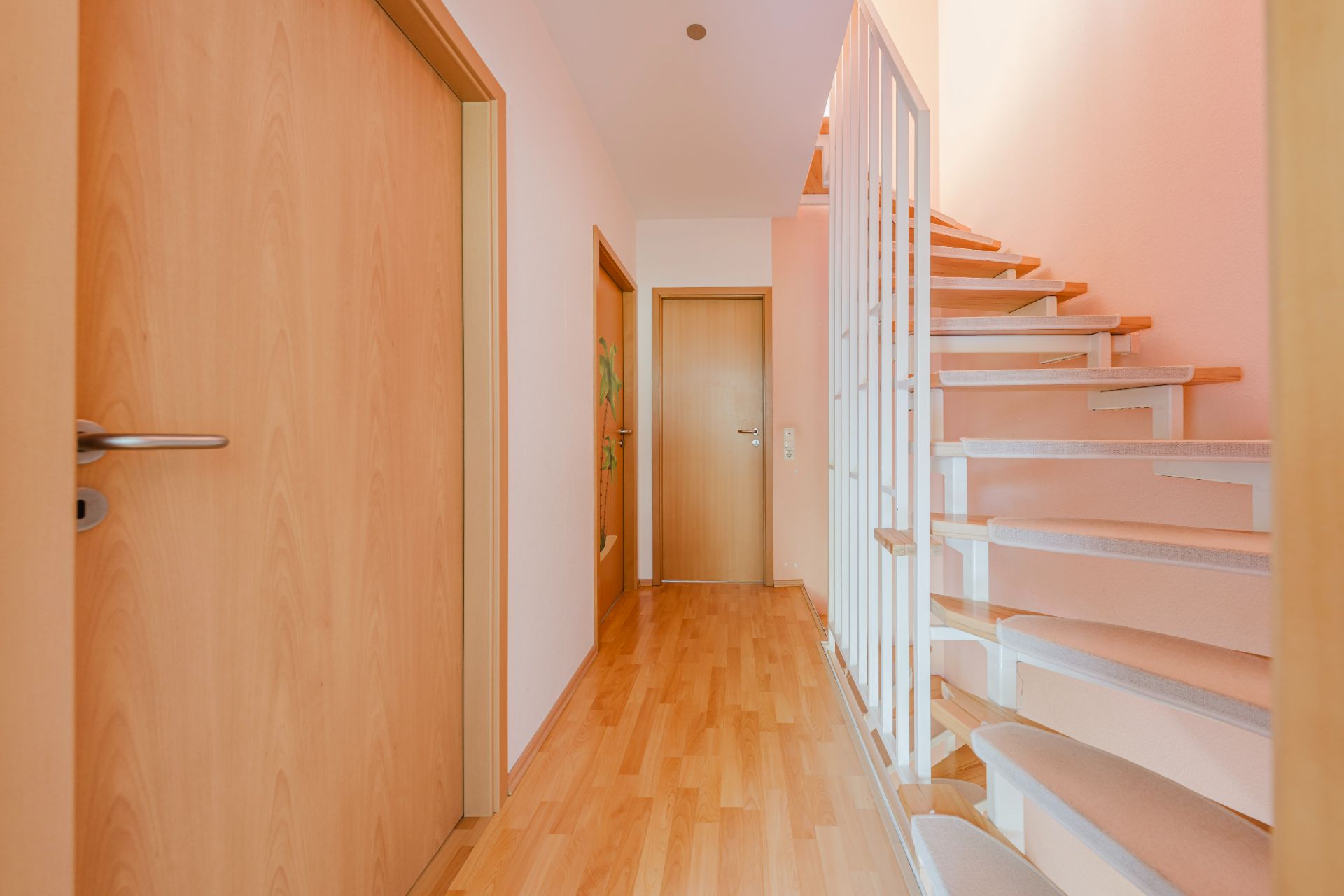 Heller Flur mit Holztüren, Holzfußboden und Treppe mit weißem Geländer.