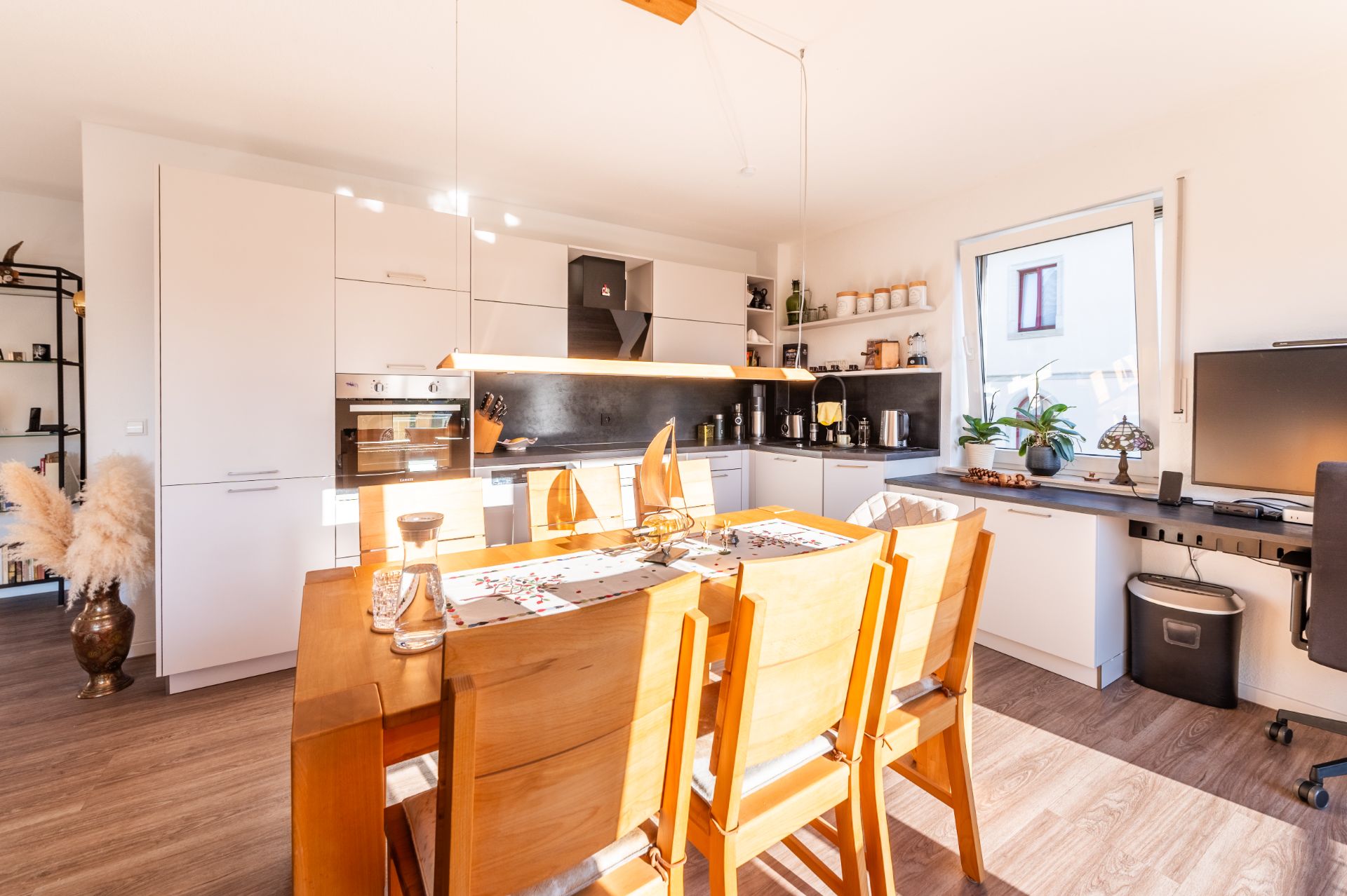 Helle, moderne Wohnküche mit Esstisch, Stühlen und Schreibtisch am Fenster.