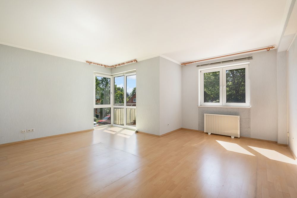 Helles, leeres Zimmer mit Parkettboden, zwei großen Fenstern und Blick ins Grüne.