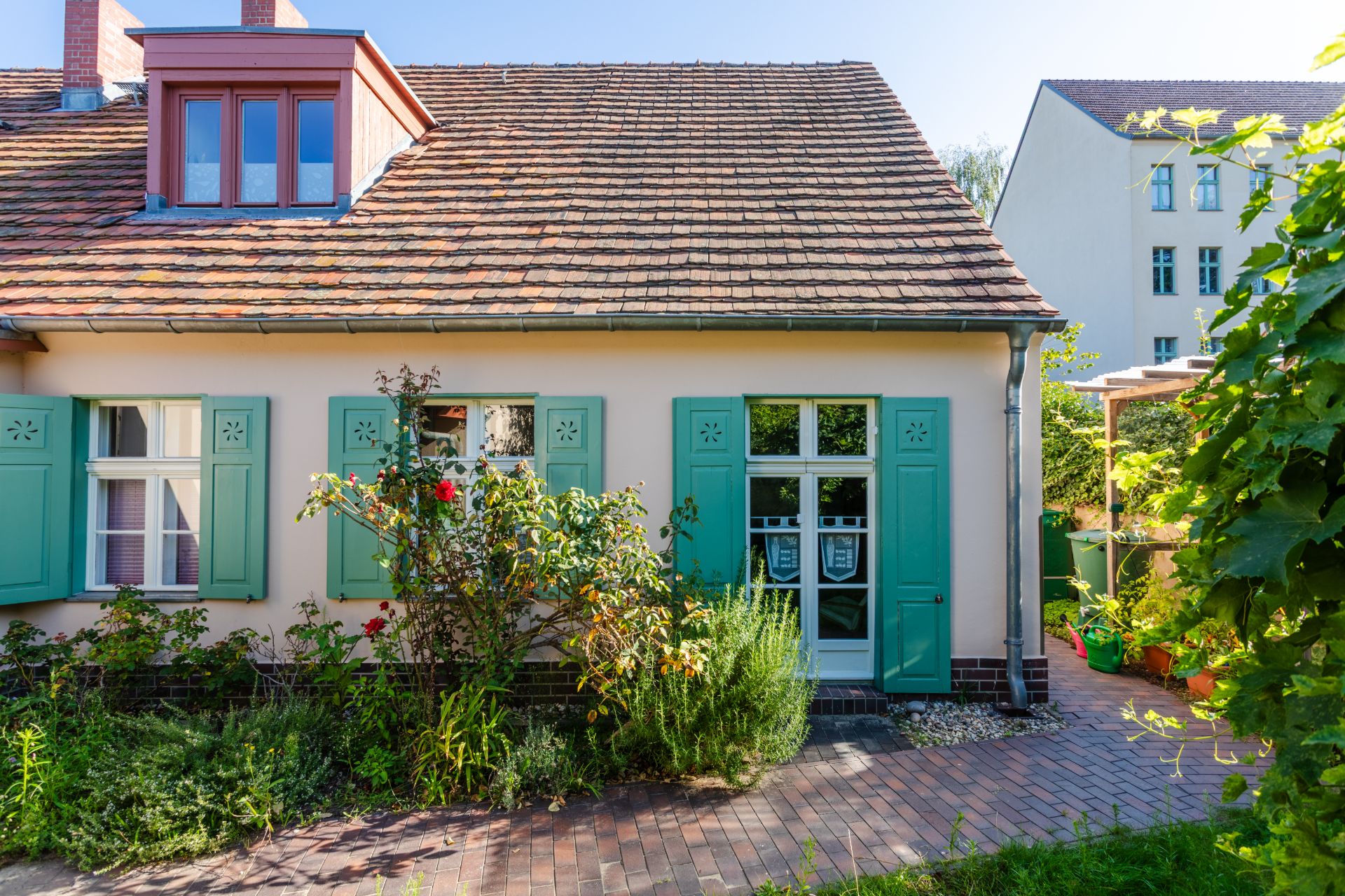 Gemütliches Haus mit grünem Fensterläden, Garten und gepflastertem Weg im Vordergrund.
