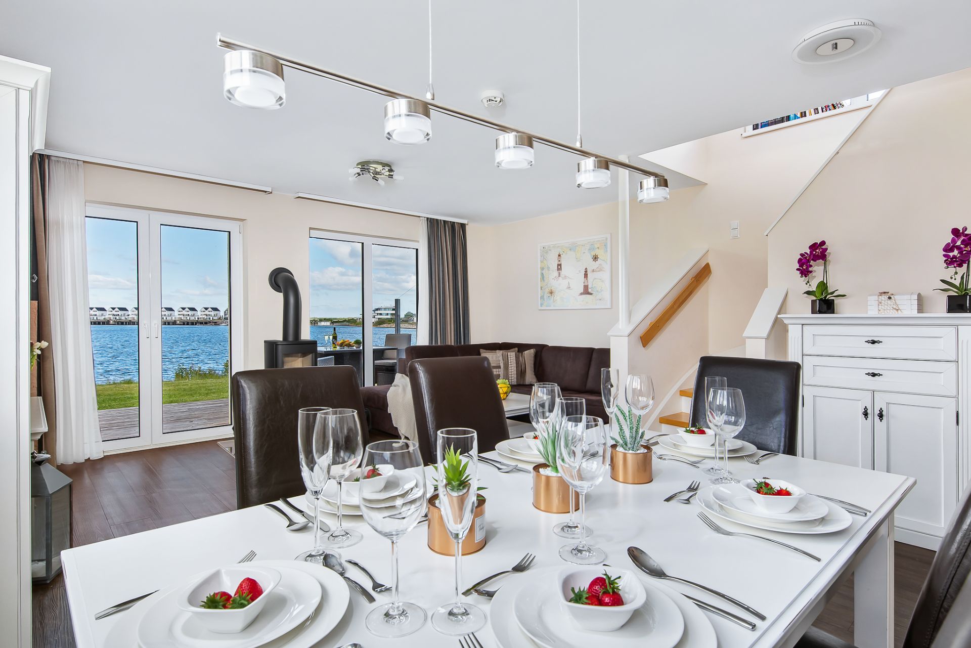 Modernes Ess- und Wohnzimmer mit gedecktem Tisch, großen Fenstern und Blick auf das Wasser.