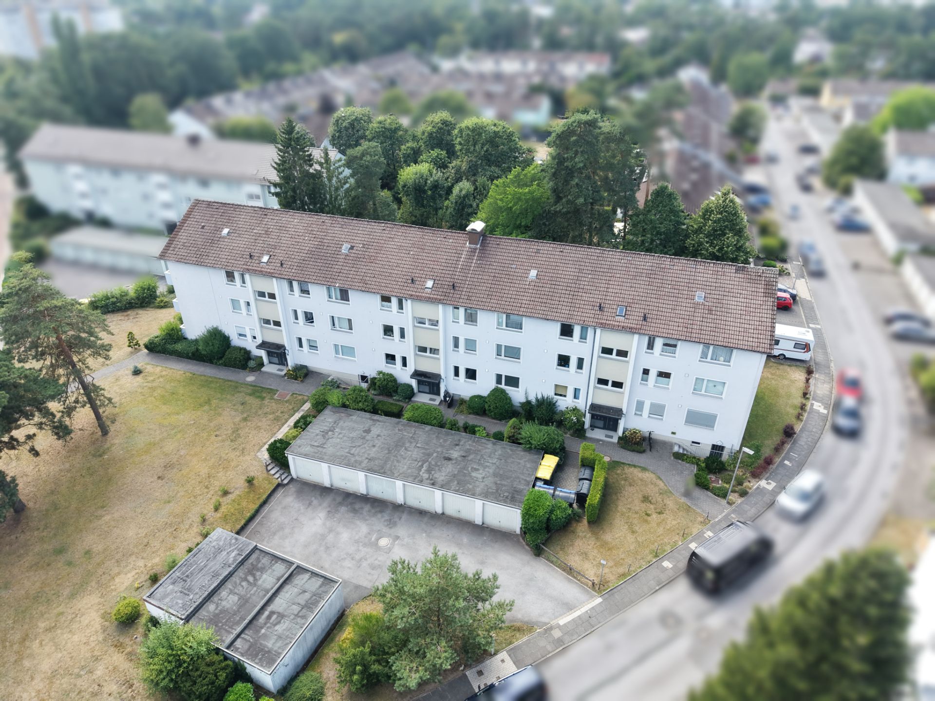 Drohnenaufnahme eines mehrstöckigen Wohnhauses mit Garagen und Gartenbereich.