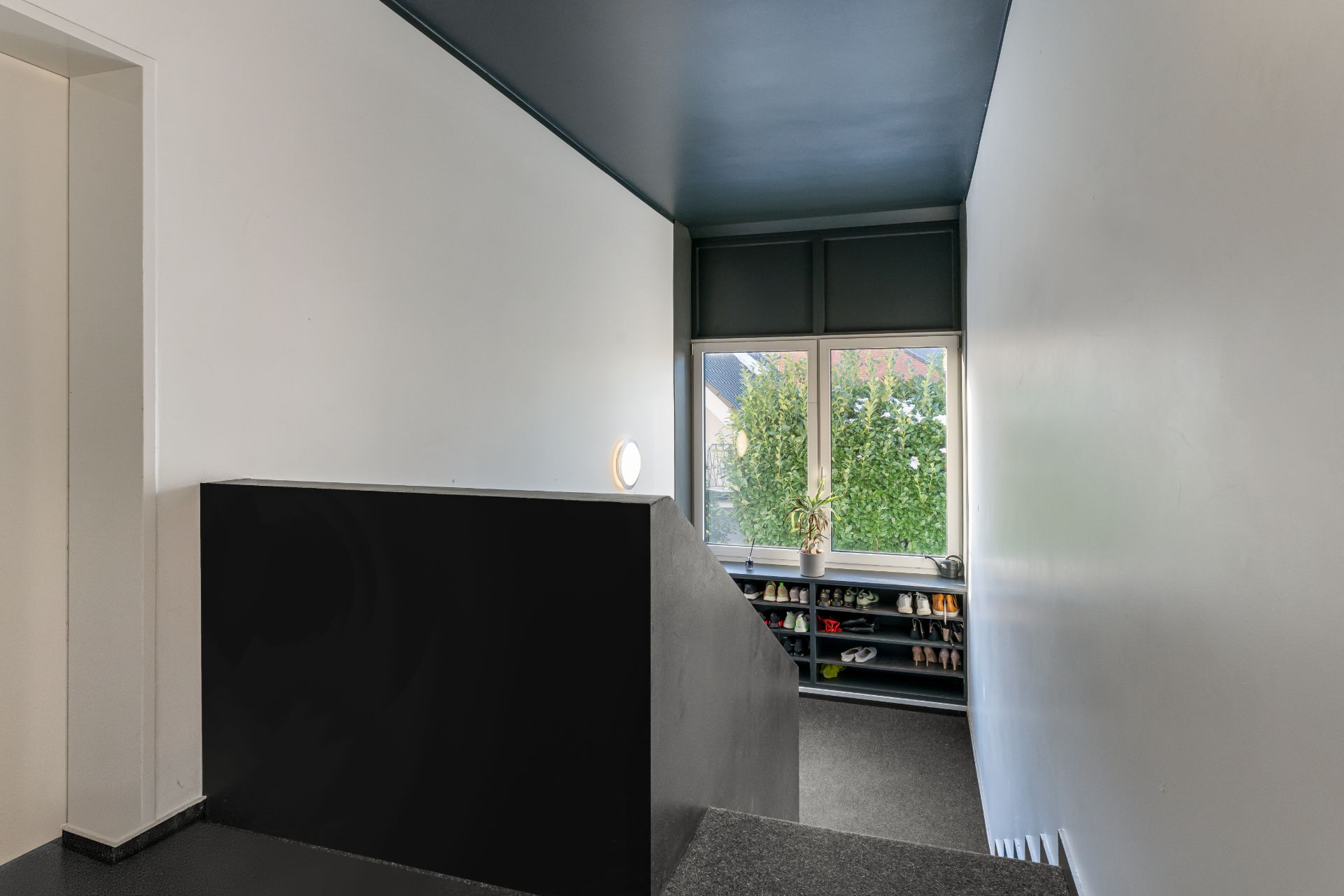 Heller Flur mit Fenster, Regal mit Schuhen und grünem Ausblick.