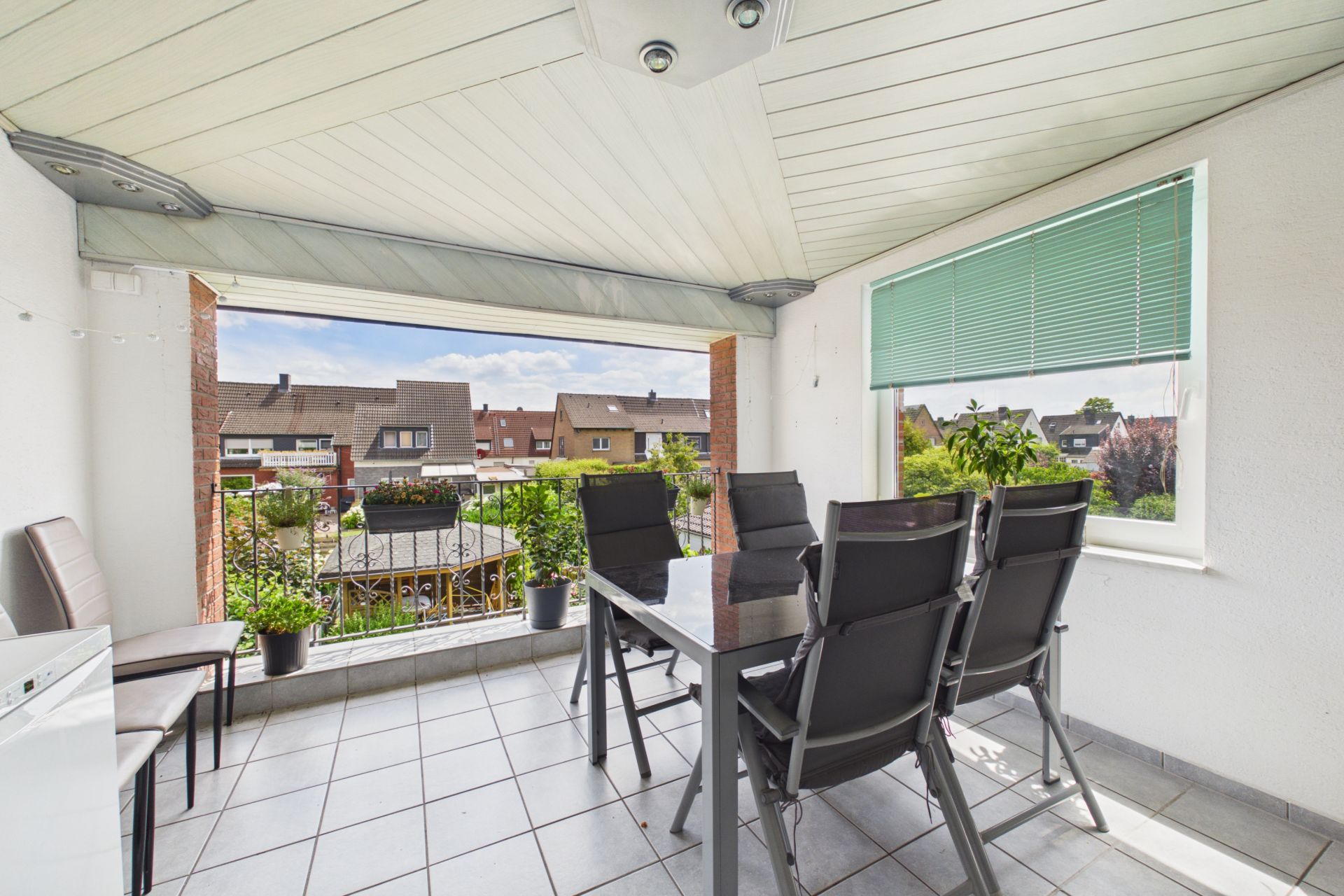 Überdachte Terrasse mit Esstisch, sechs Stühlen und Blick auf Nachbarhäuser.