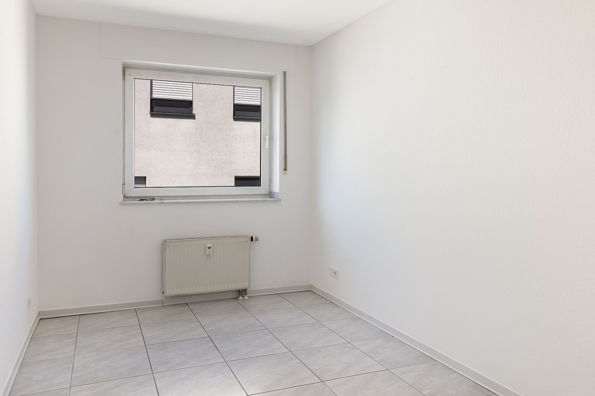 Leerer Raum mit weißem Wänden, Fliesenboden, Heizkörper und Fenster.
