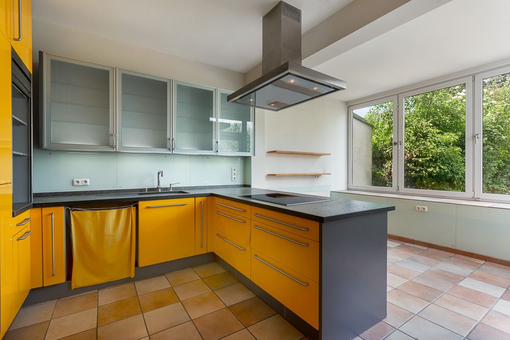 Moderne Küche mit gelben Schränken, großem Fenster und Kochinsel, Fliesenboden.