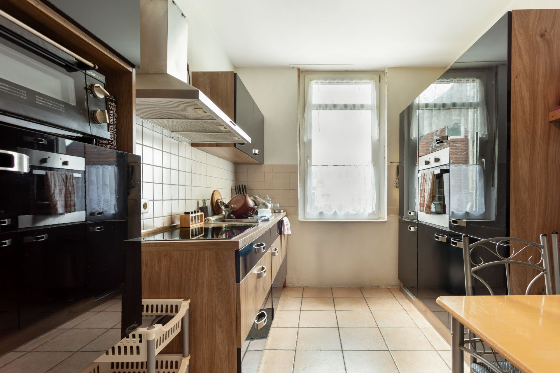 Moderne Küche mit Holzschränken, Herd, Spüle und Fenster, Fliesenboden und Esstisch.