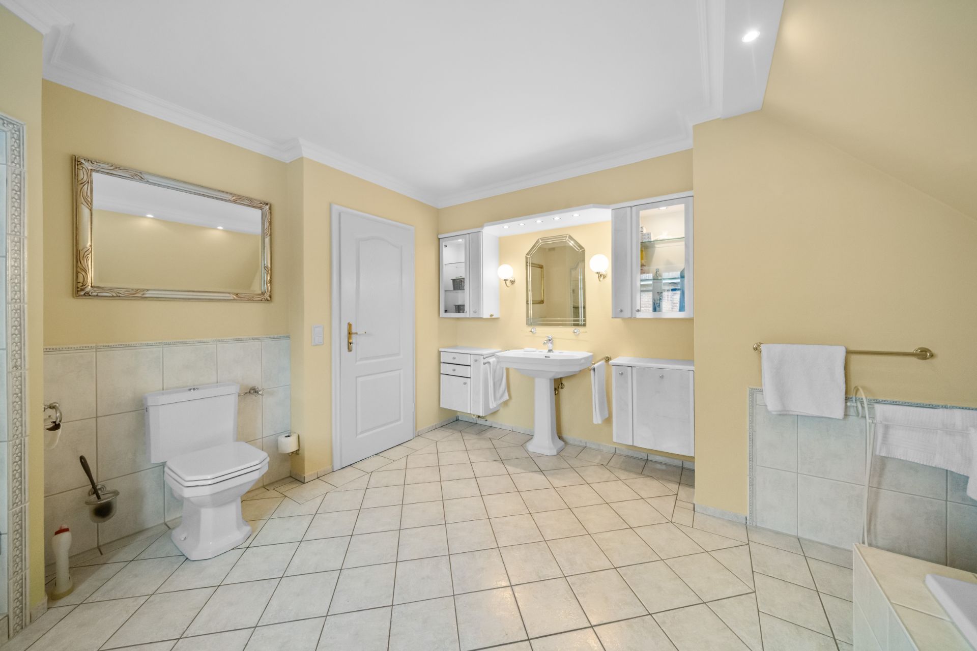 Helles Badezimmer mit Toilette, Waschbecken, Spiegeln und Handtuchhaltern auf gefliestem Boden.