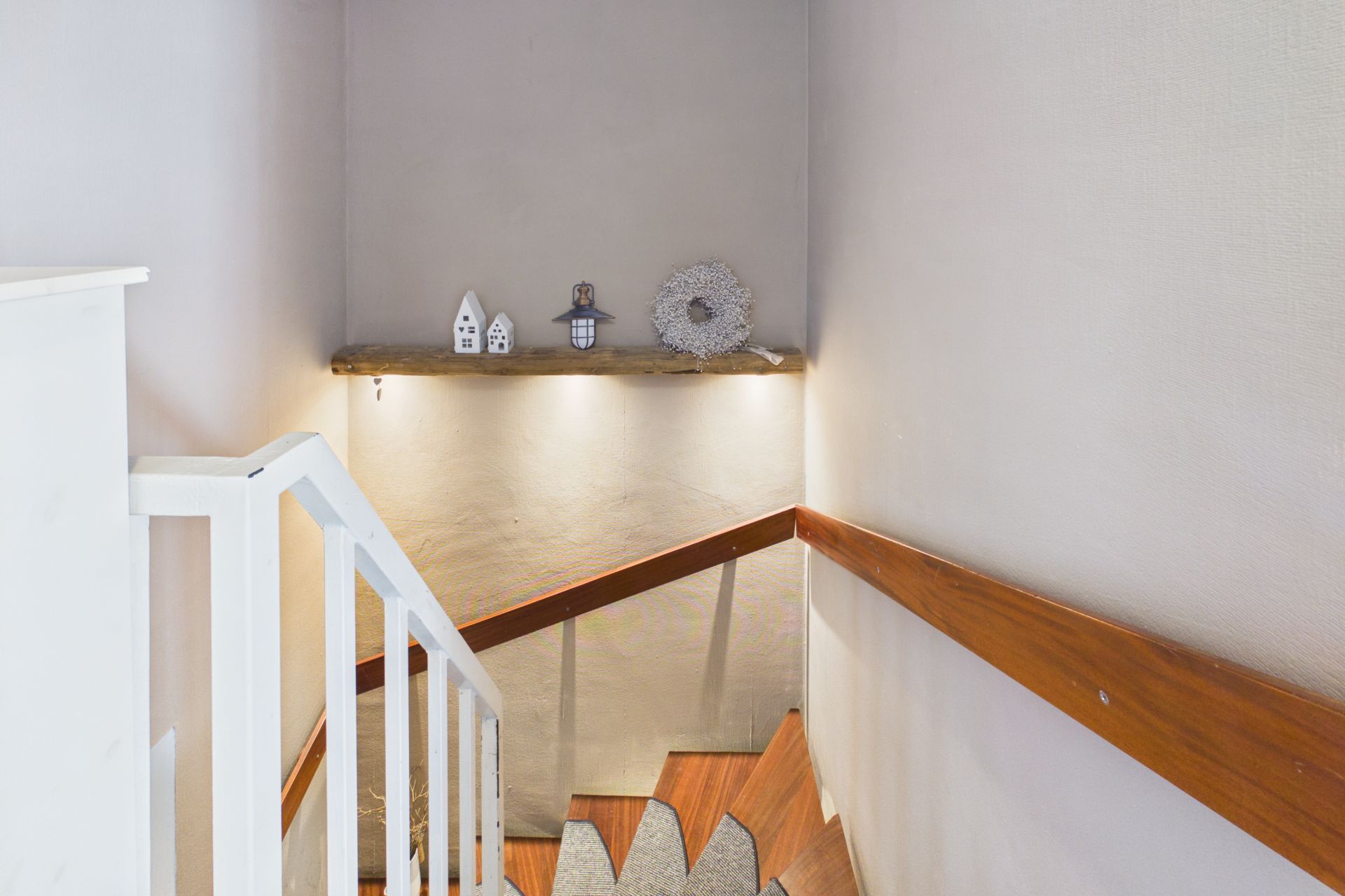 Treppe mit weißem Geländer und kleinem dekoriertem Regal an der Wand.