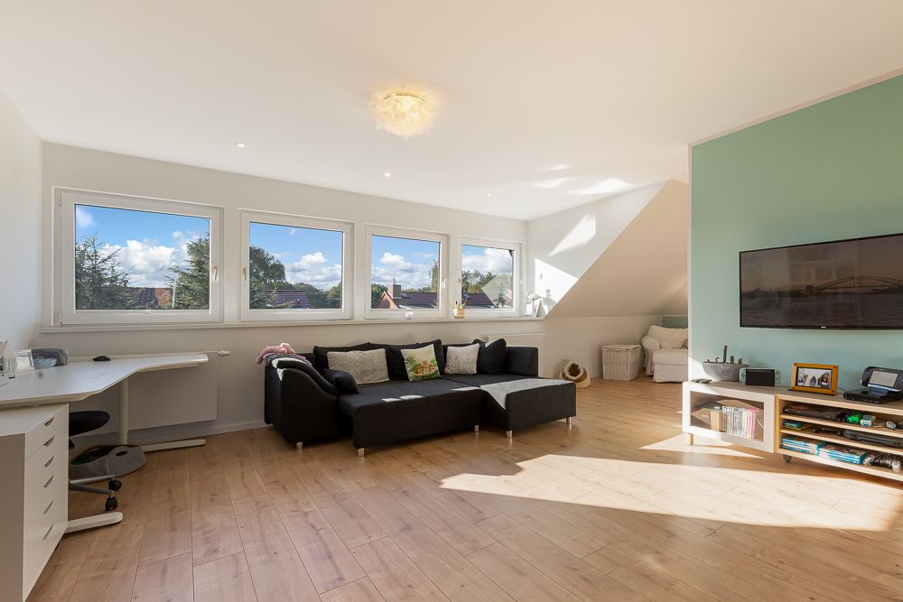 Helles Wohnzimmer mit Ecksofa, Schreibtisch, Holzfußboden und großem Fenster.
