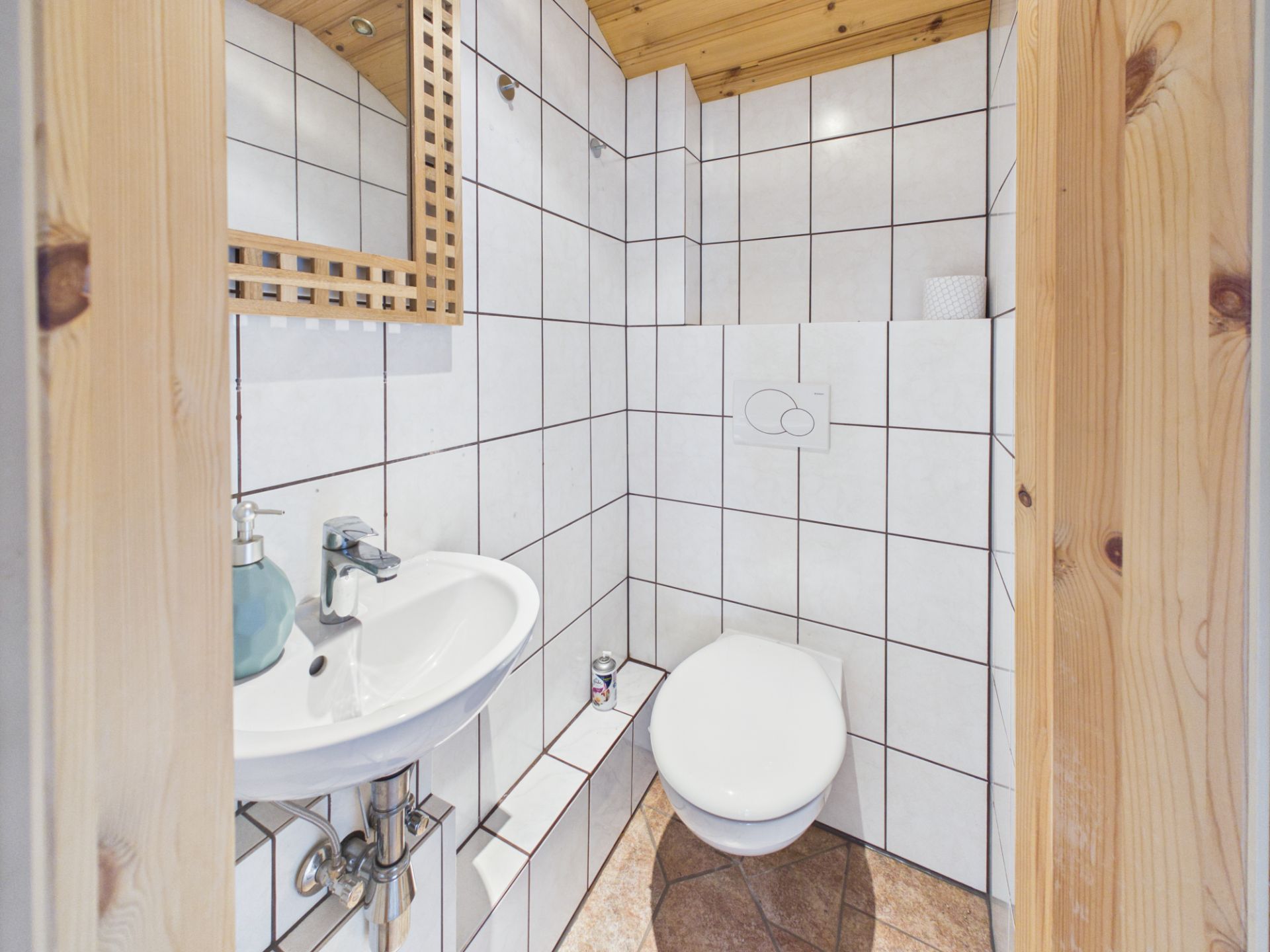 Kleines Badezimmer mit weiß gefliesten Wänden, WC, Waschbecken und Spiegel.