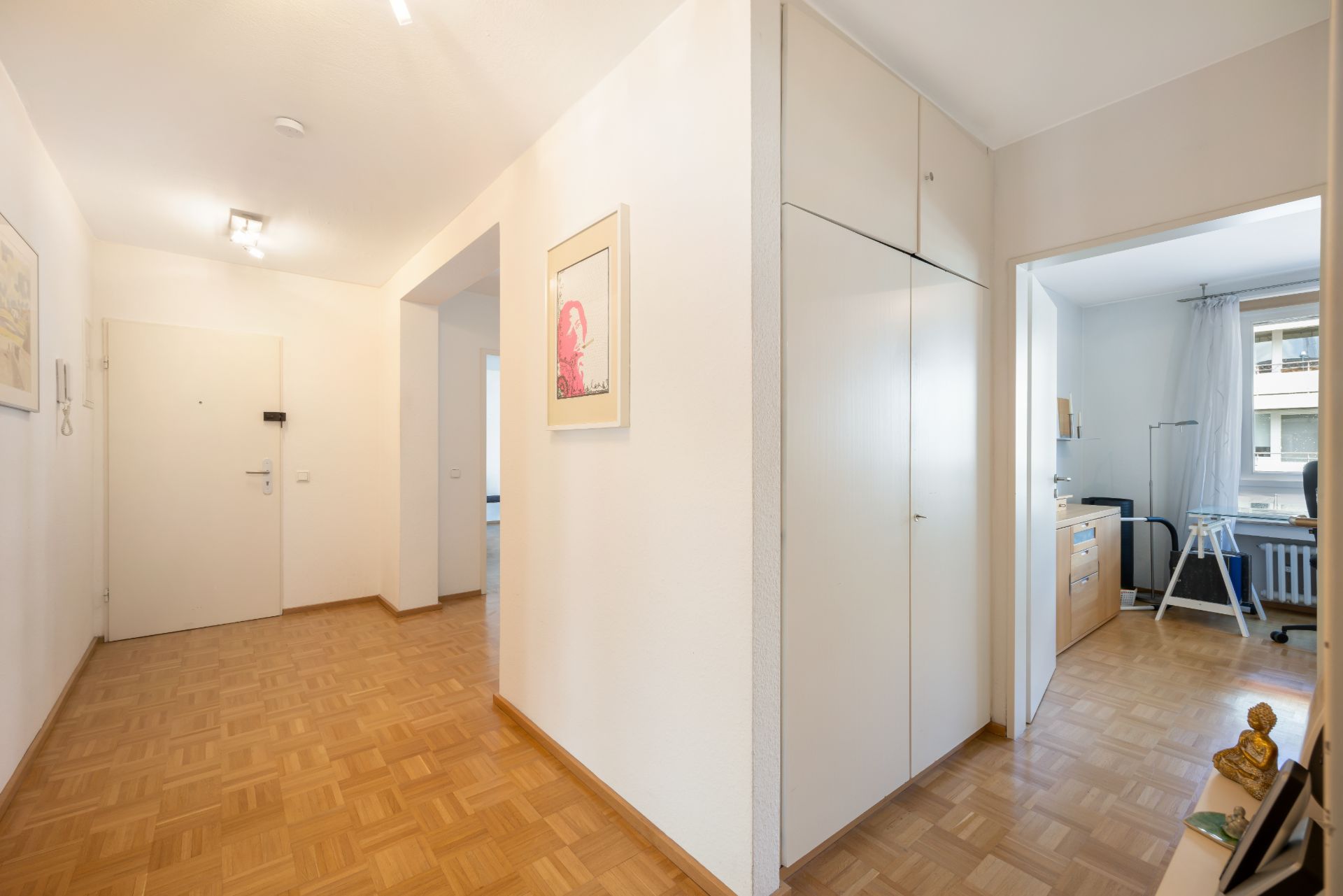 Heller Flur mit Parkettboden, Einbauschränken und Blick in ein Arbeitszimmer.