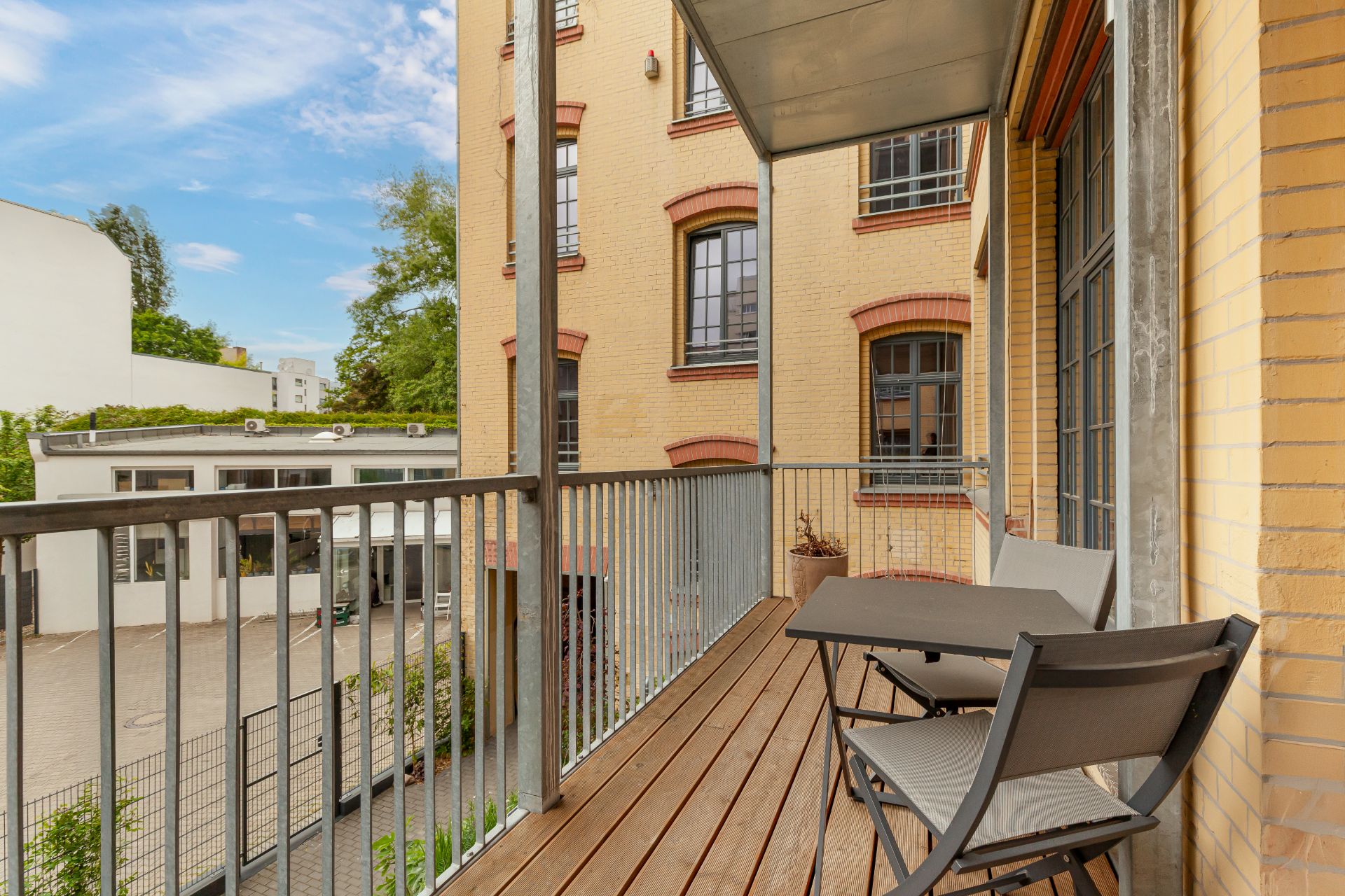 Balkon mit zwei Stühlen und einem Tisch, Blick auf Innenhof und gelbes Wohngebäude.