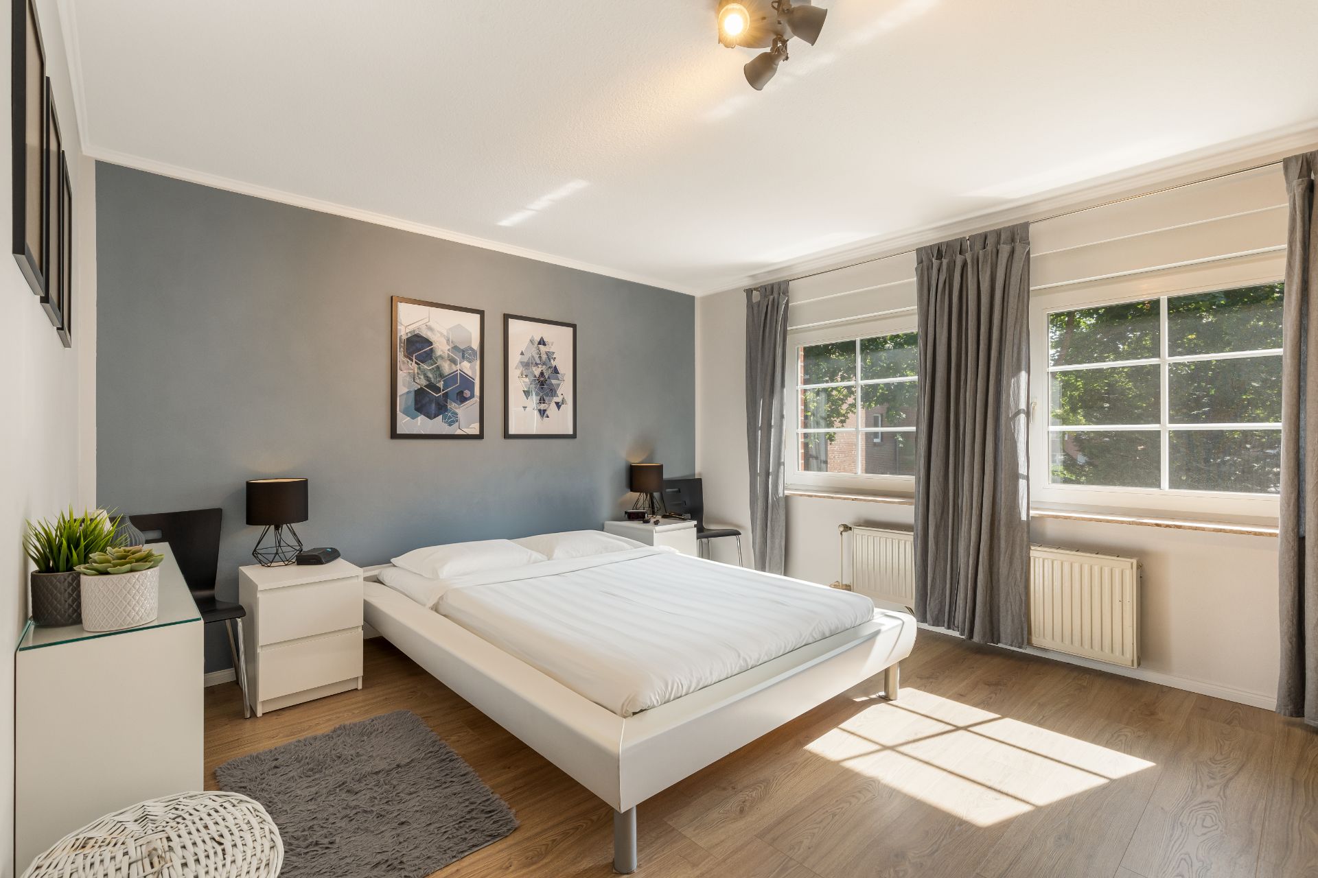 Helles Schlafzimmer mit großem Bett, zwei Fenstern und moderner Dekoration.