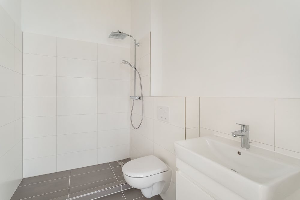 Modernes, weiß gefliestes Badezimmer mit Dusche, Toilette und Waschbecken.